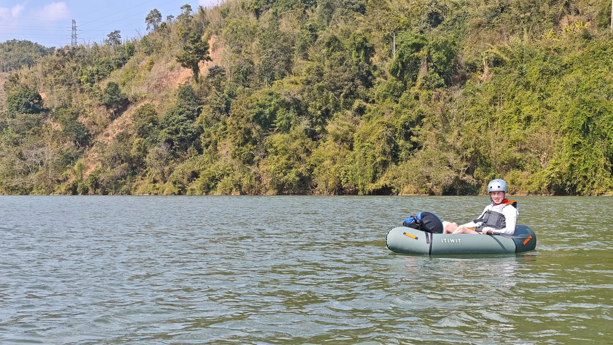 Close water-level view of a paddler in an Itiwit packraft with dry bag on the Nam Ou river at Muang Khua with boats and town on the hillside