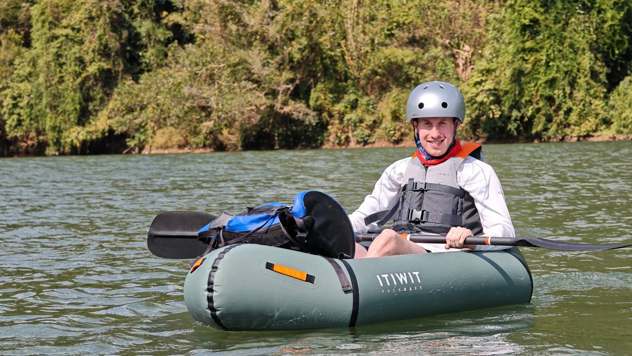 Paddler smiling in an Itiwit packraft on the Nam Ou river at Muang Khua with lush green vegetation along the banks
