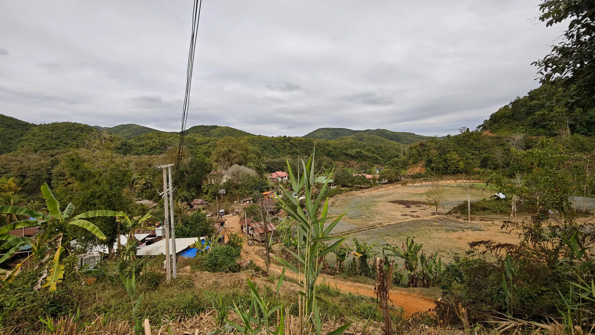 Panoramic hilltop view over Ban Haddean village with banana palms, tin-roofed houses and forested mountains along the Nam Ou valley