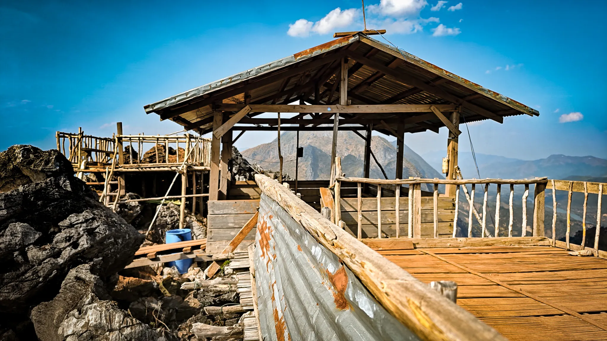 Rustic wooden shelter and viewing platform at the summit of Pha Kew Lom with mountains in the background