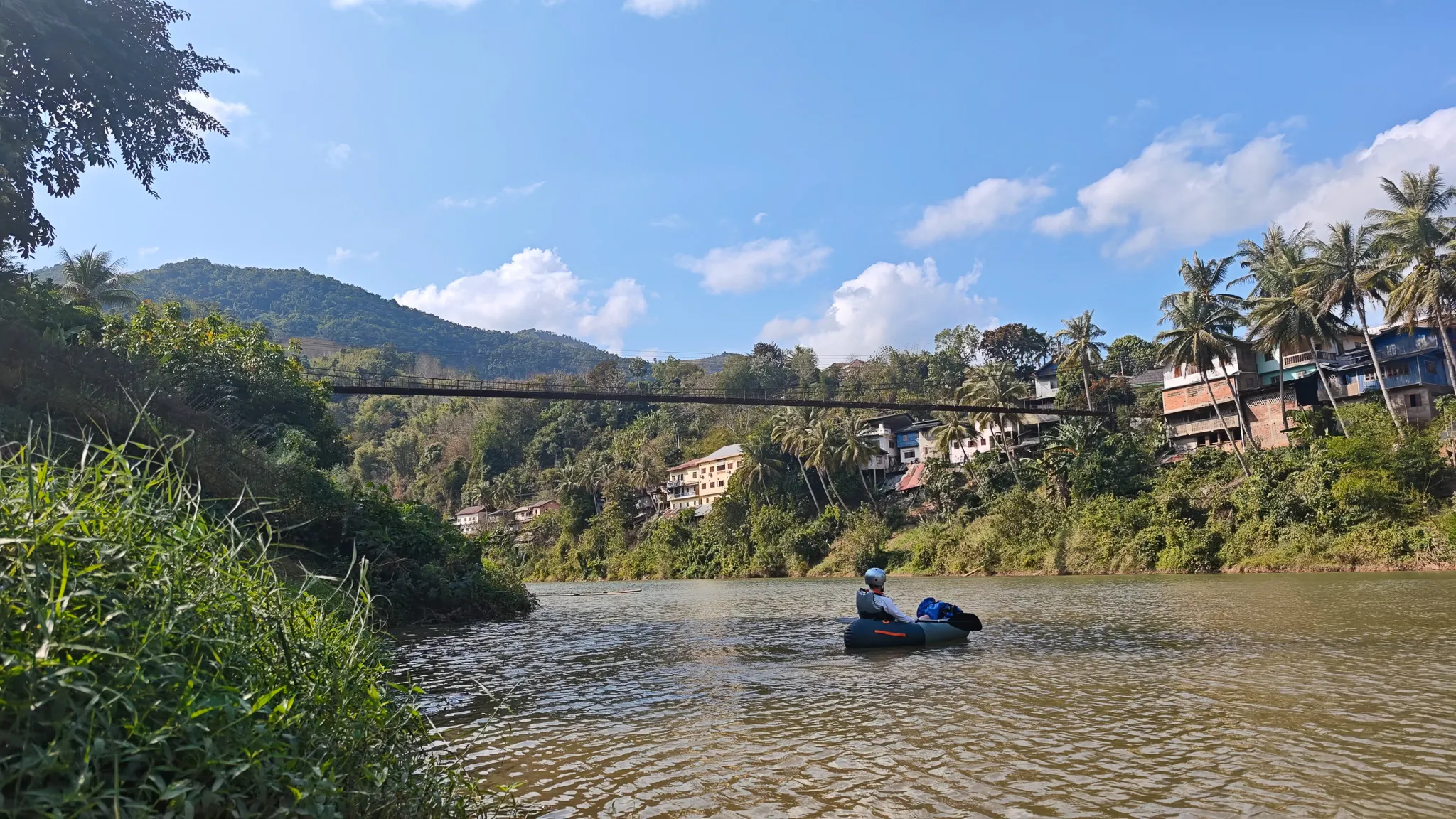Paddler leaning back and relaxing in an Itiwit packraft on the Nam Ou river beneath the Muang Khua suspension bridge with orange life jacket