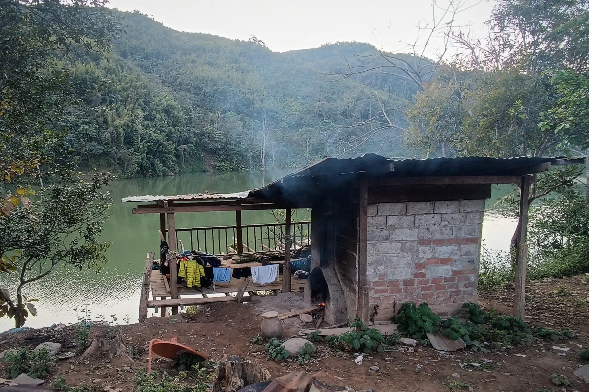 Abandoned shelter with brick oven and clothes hanging to dry overlooking the Nam Ou river surrounded by misty mountains