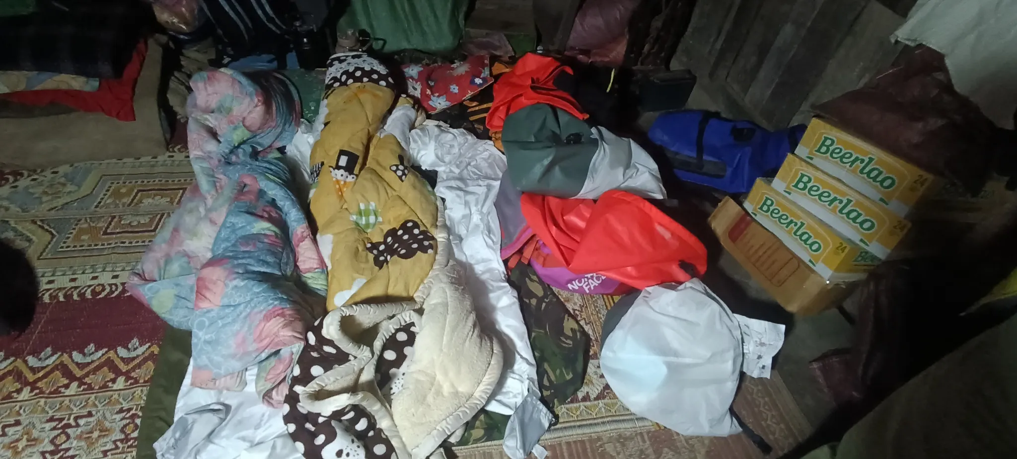 Blankets and sleeping bags laid out on the floor of a village house in Ban Haddean with Beerlao cartons stacked beside the bedding
