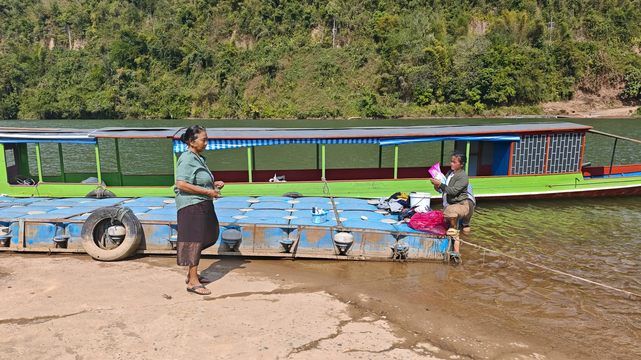 Traditional Lao longboat moored on the sandy bank of the Nam Ou river in Muang Khua with a local woman walking past