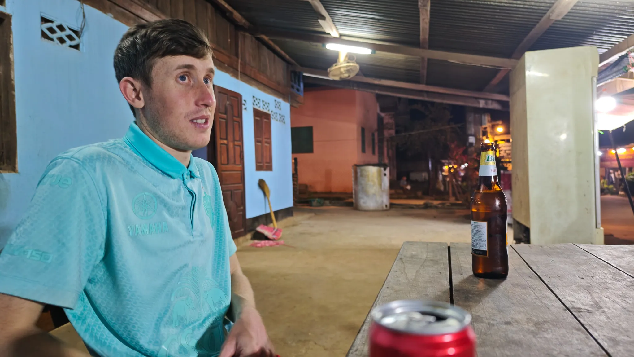 Traveller sitting at a wooden table with Beer Lao bottles at a guesthouse in Muang Ngoi at night