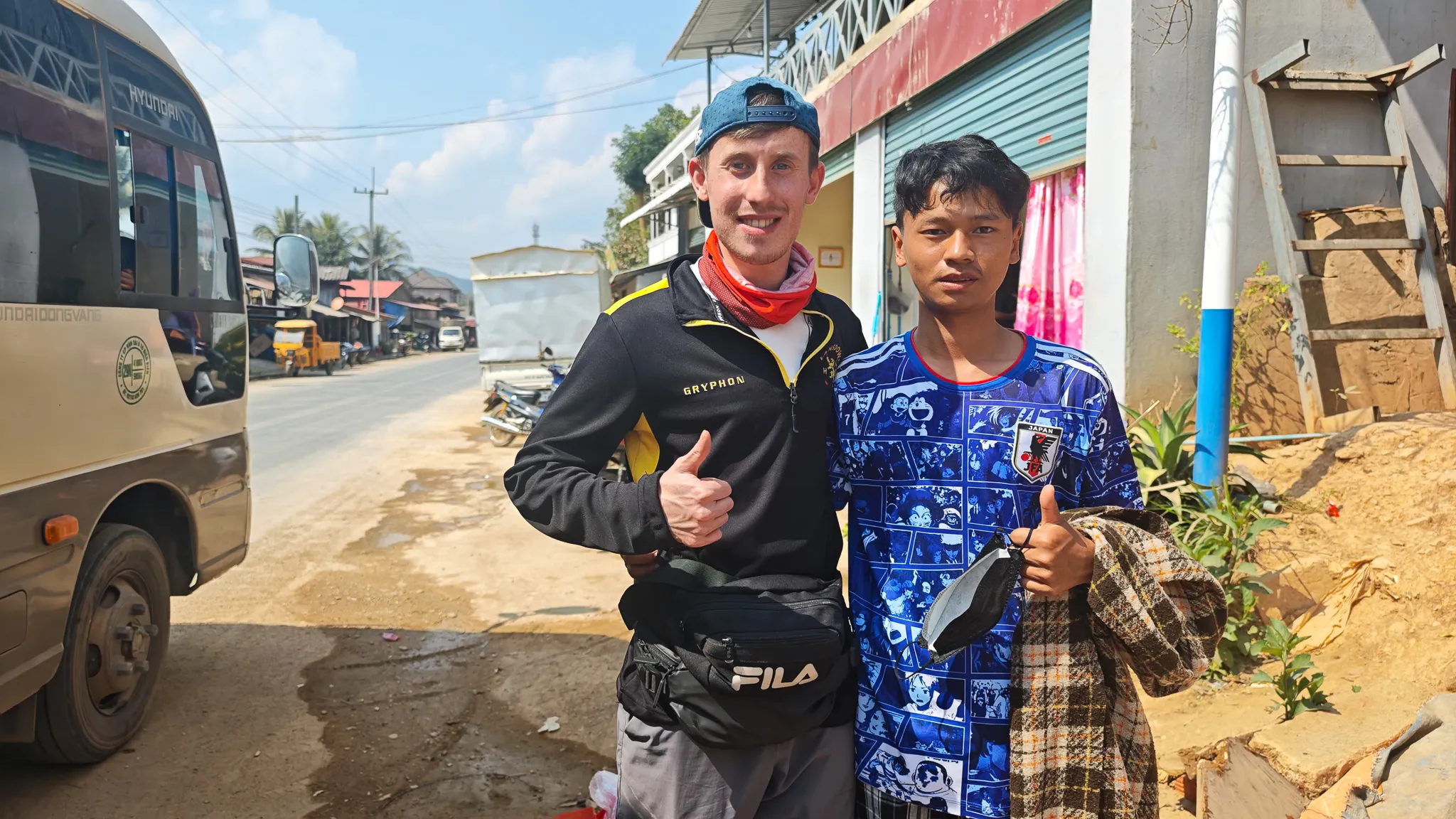 Traveller and local both giving thumbs up at a village stop on the bus route through northern Laos towards Muang Khua