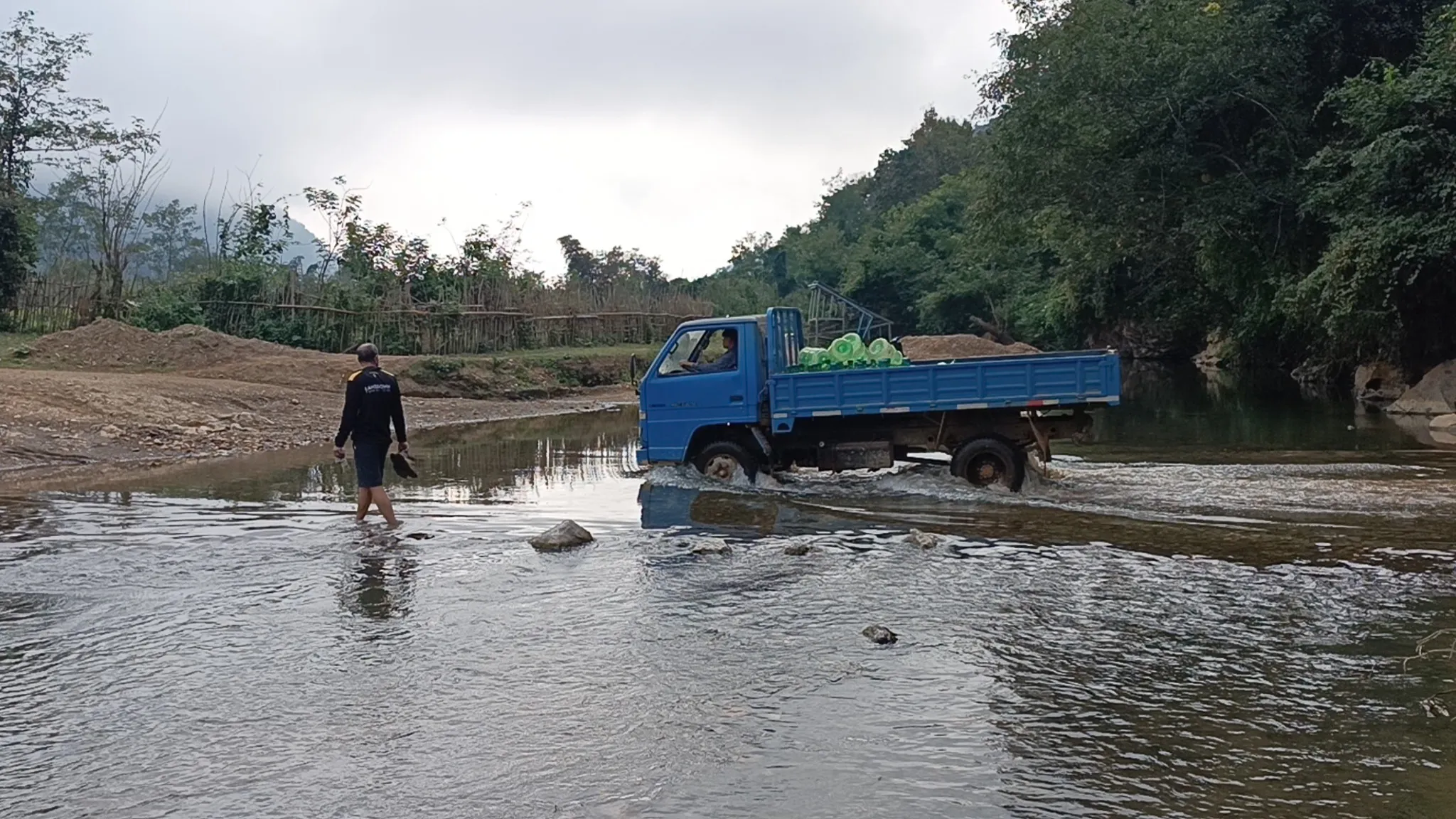 Blue truck and a man fording a shallow river on the way back from the cave near Muang Ngoi