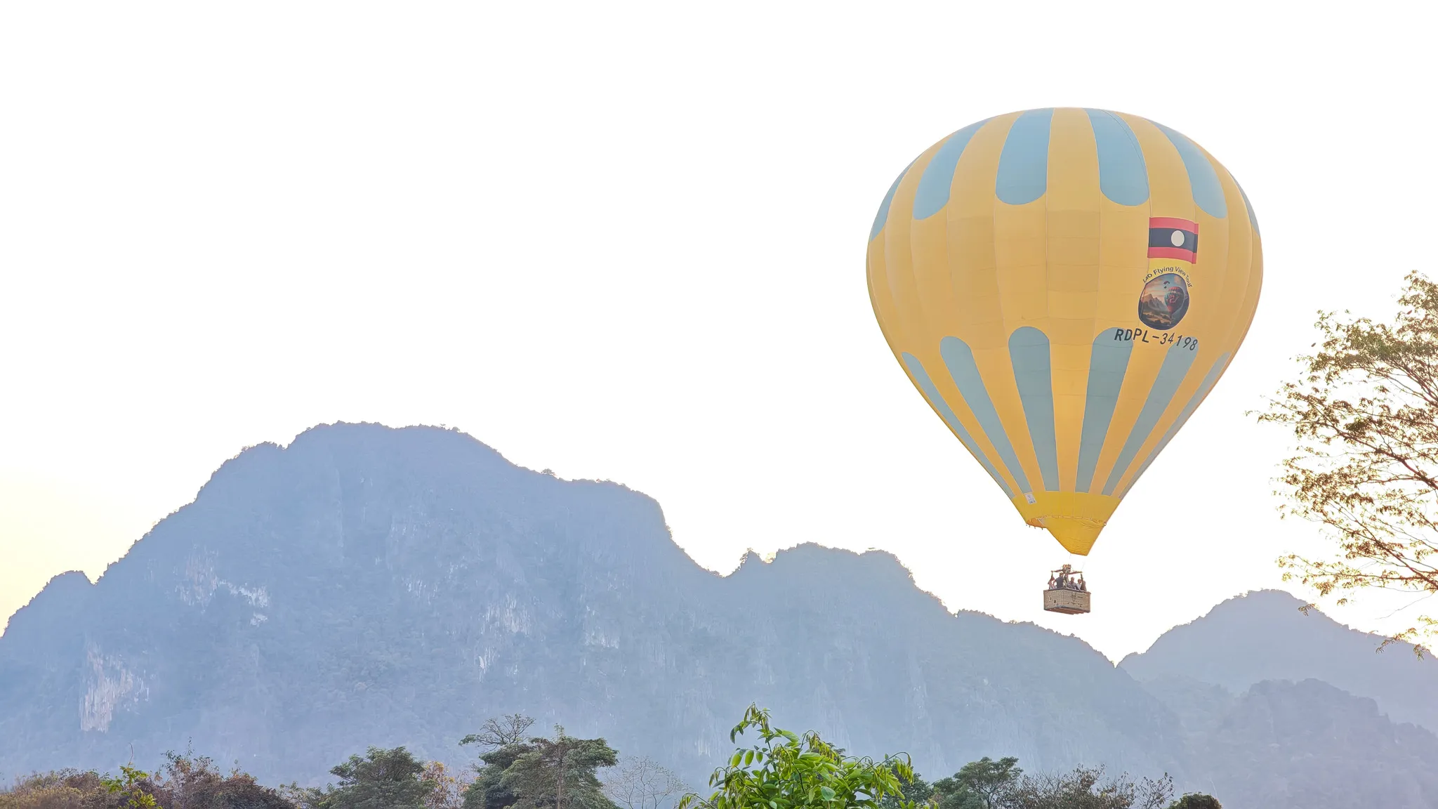 Close-up of a yellow hot air balloon with RDPL registration against misty karst peaks at sunset in Vang Vieng