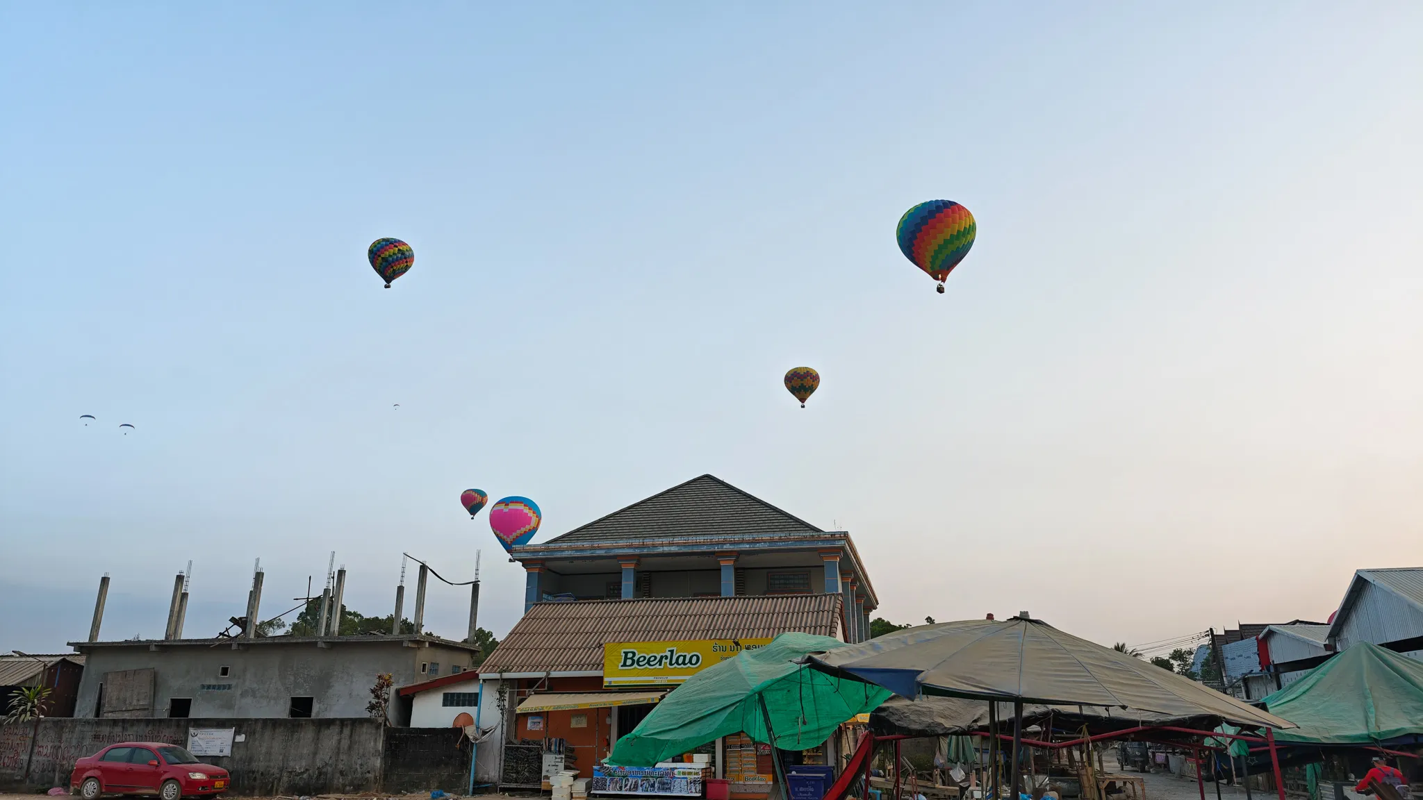 Hot air balloons and paragliders above Vang Vieng town with a Beerlao shop sign in the foreground
