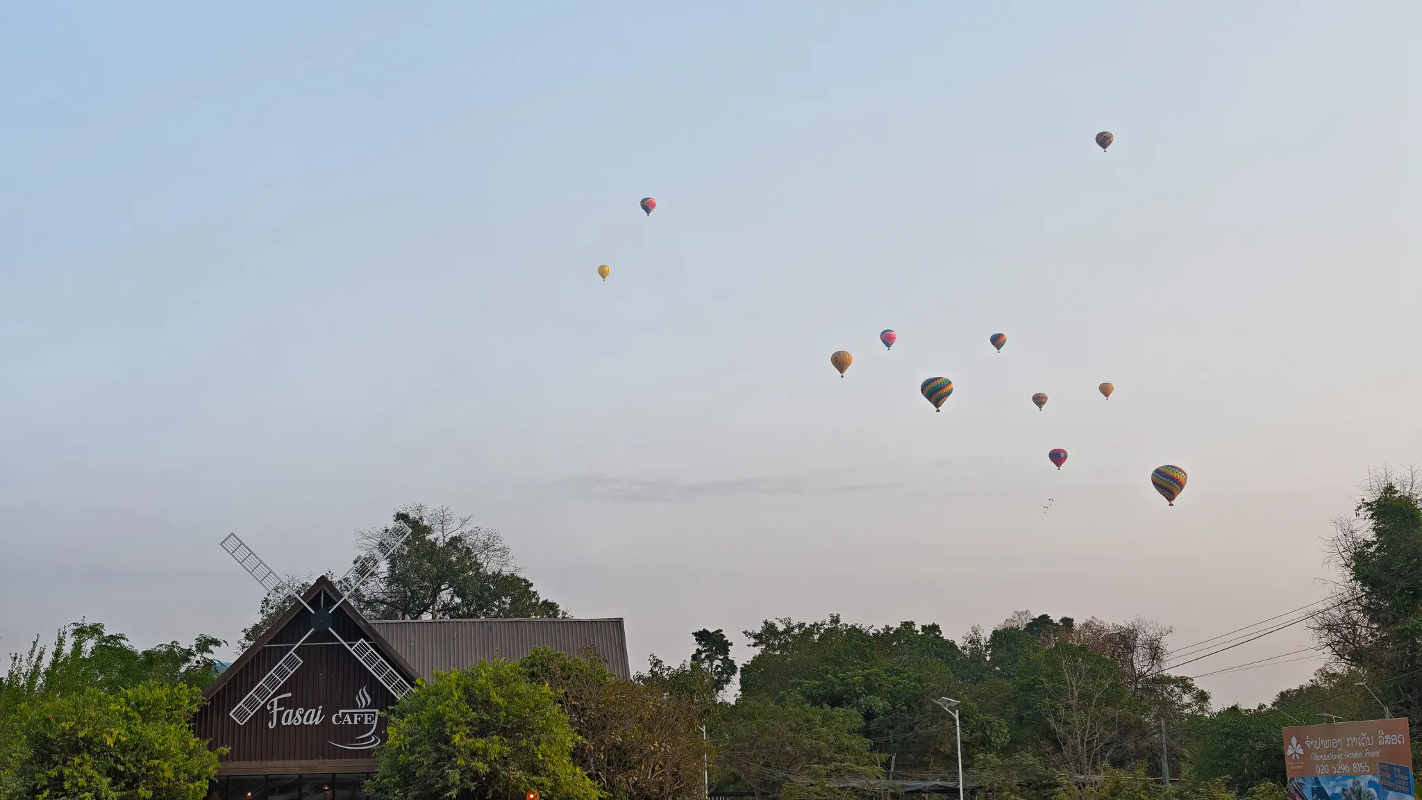 Hot air balloons floating past the Fasai Cafe windmill building at dusk in Vang Vieng