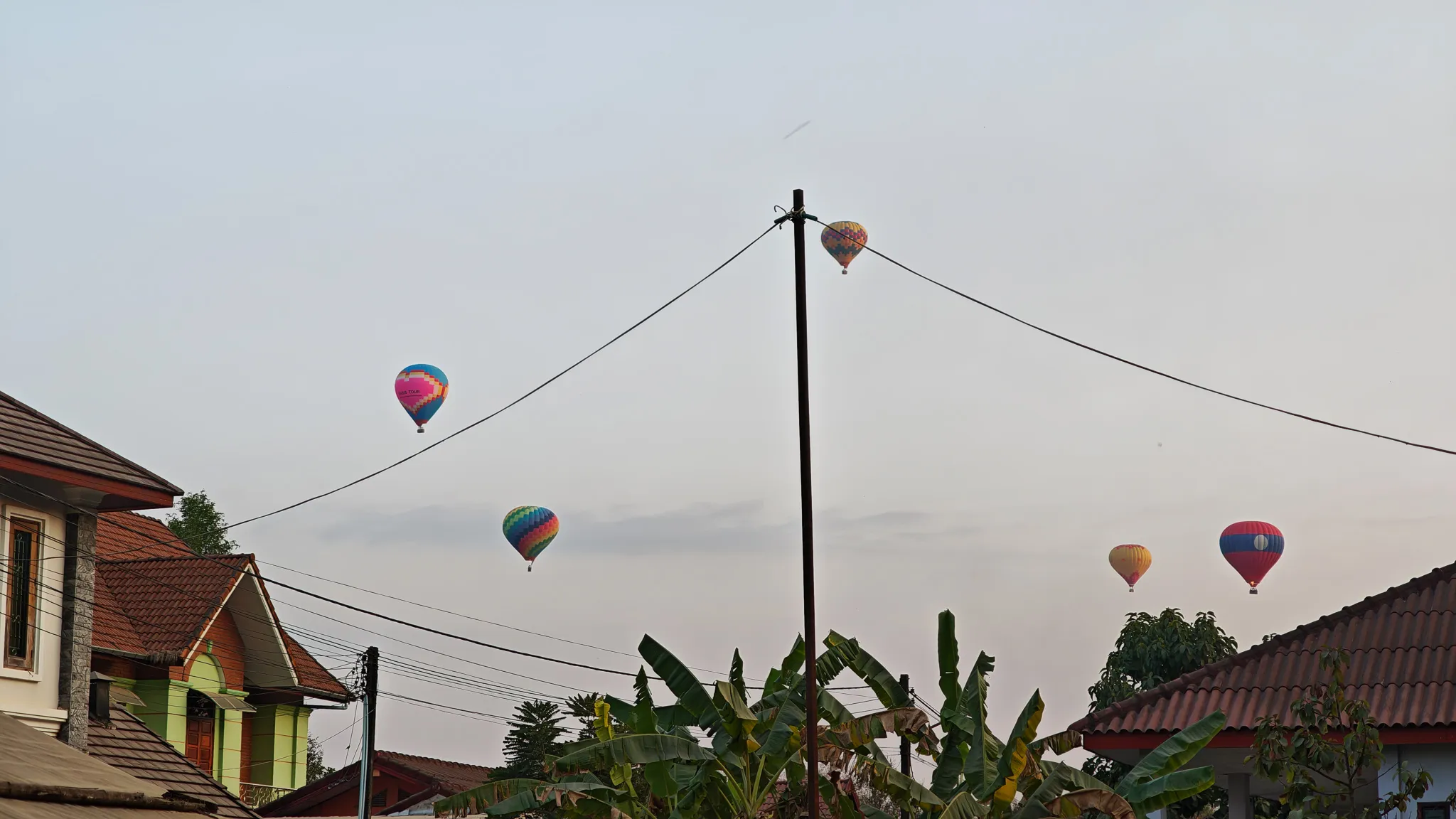 Colourful hot air balloons floating low over rooftops and banana trees in Vang Vieng town