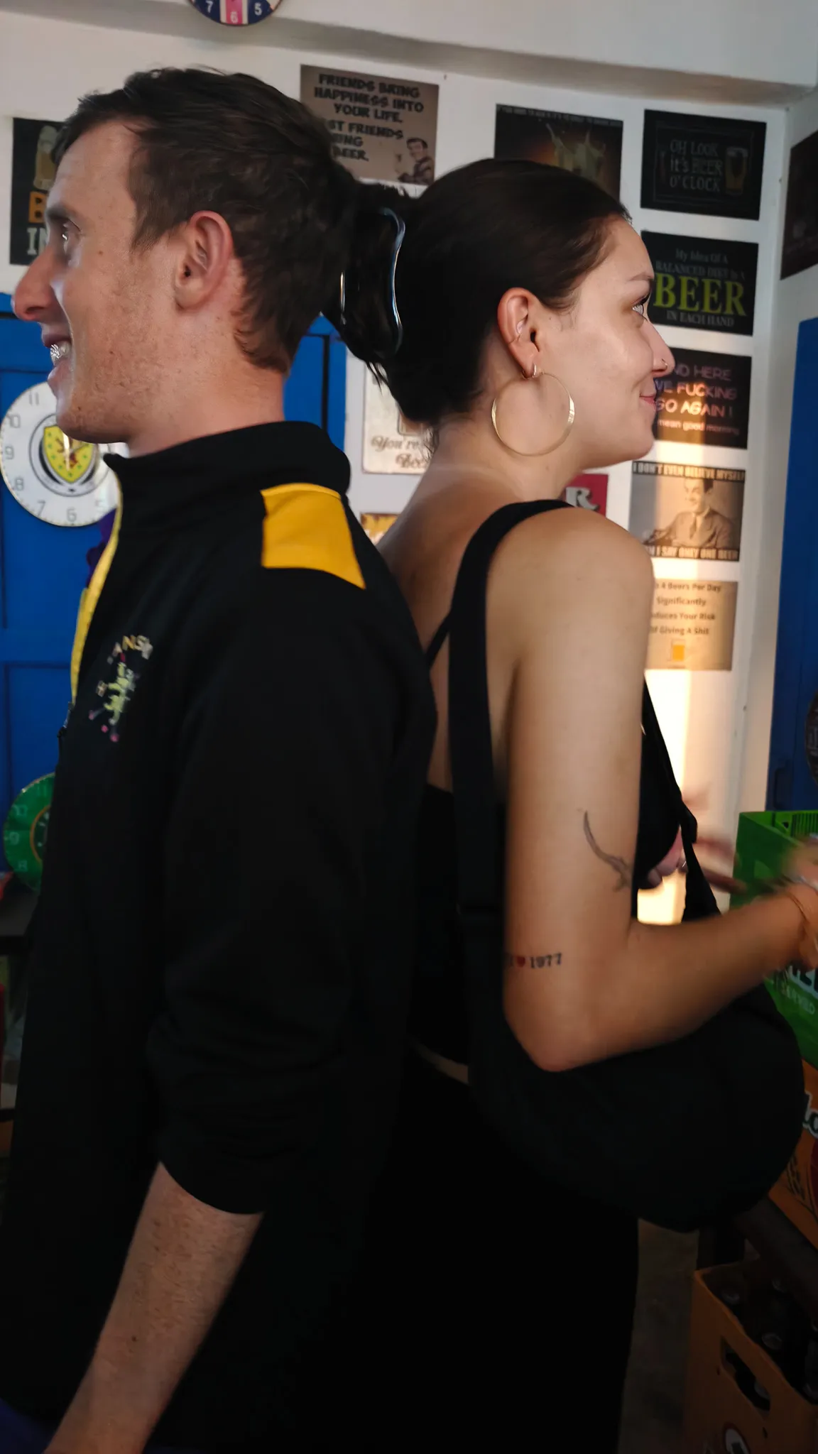 Young couple standing back to back at a bar covered in beer signs and memorabilia in Vang Vieng