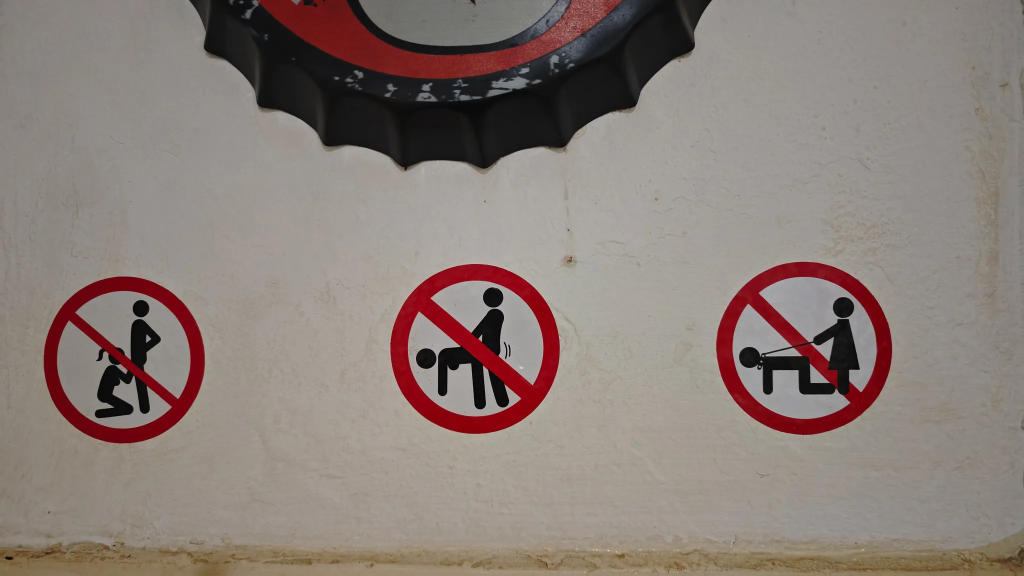 Three humorous prohibition stickers on a bar wall beneath a bottle cap mirror in Vang Vieng