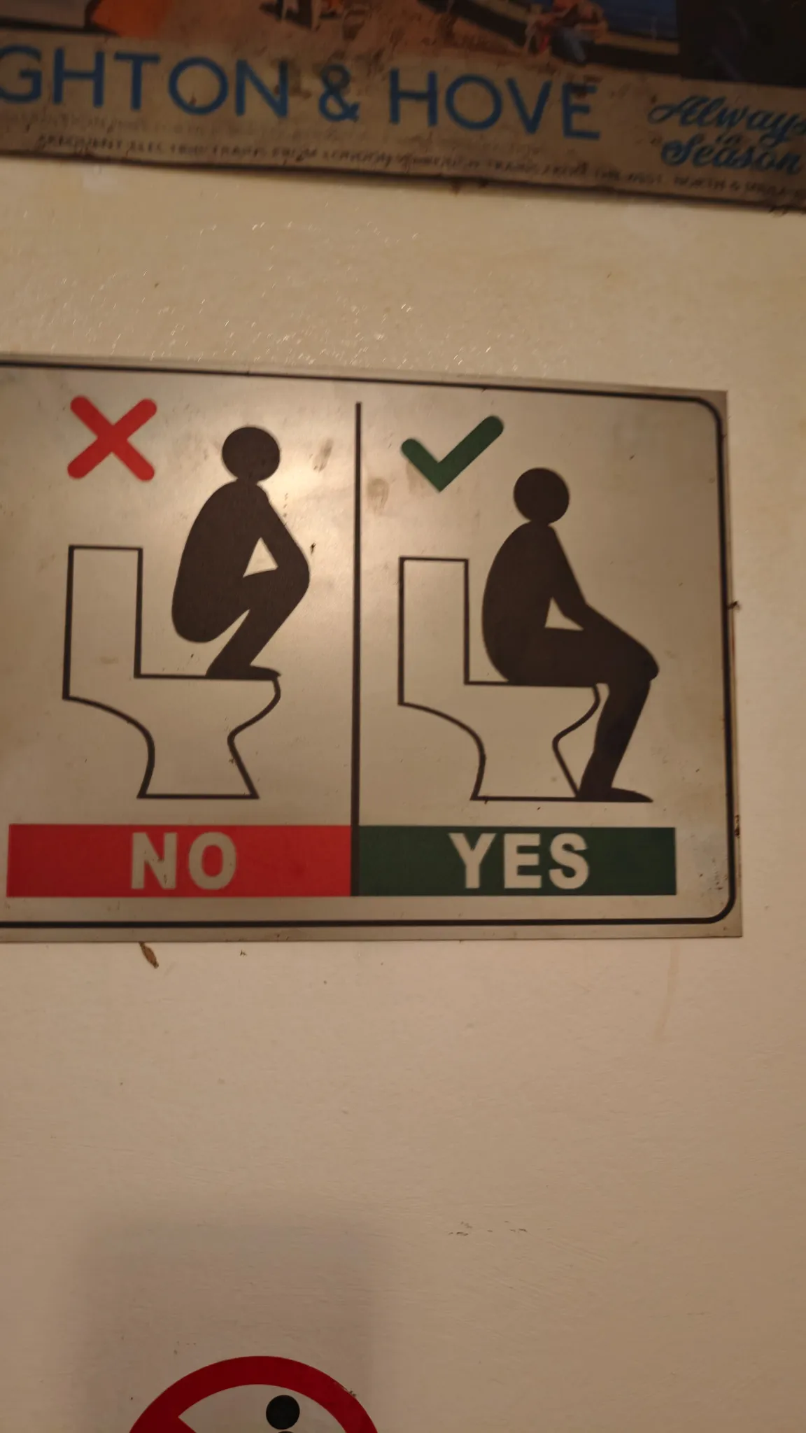 Funny bar toilet instruction sign showing how to sit properly alongside a Brighton and Hove poster in Vang Vieng