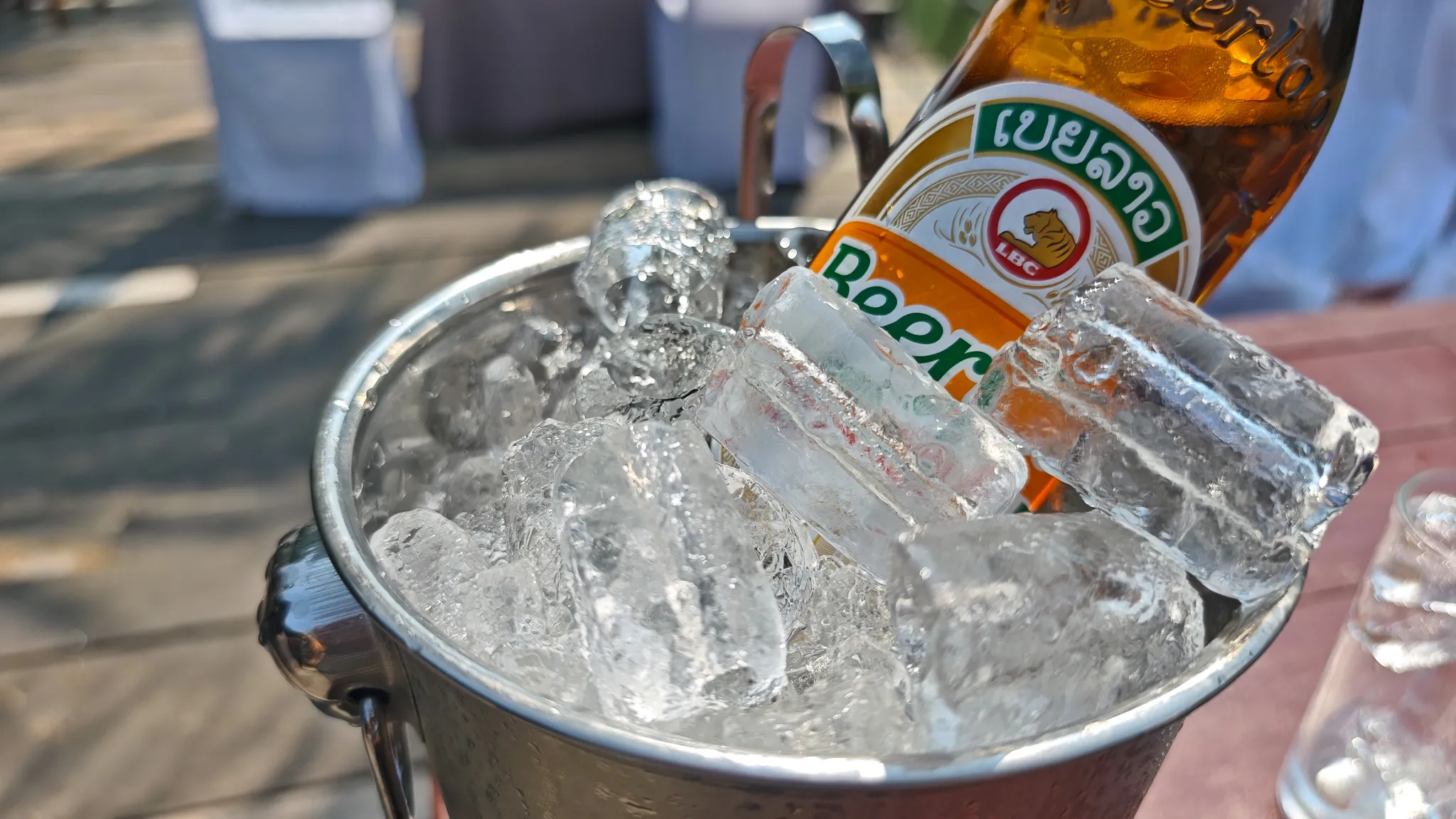 Beer Lao bottle in a metal ice bucket at a riverside bar with limestone karst views in Vang Vieng