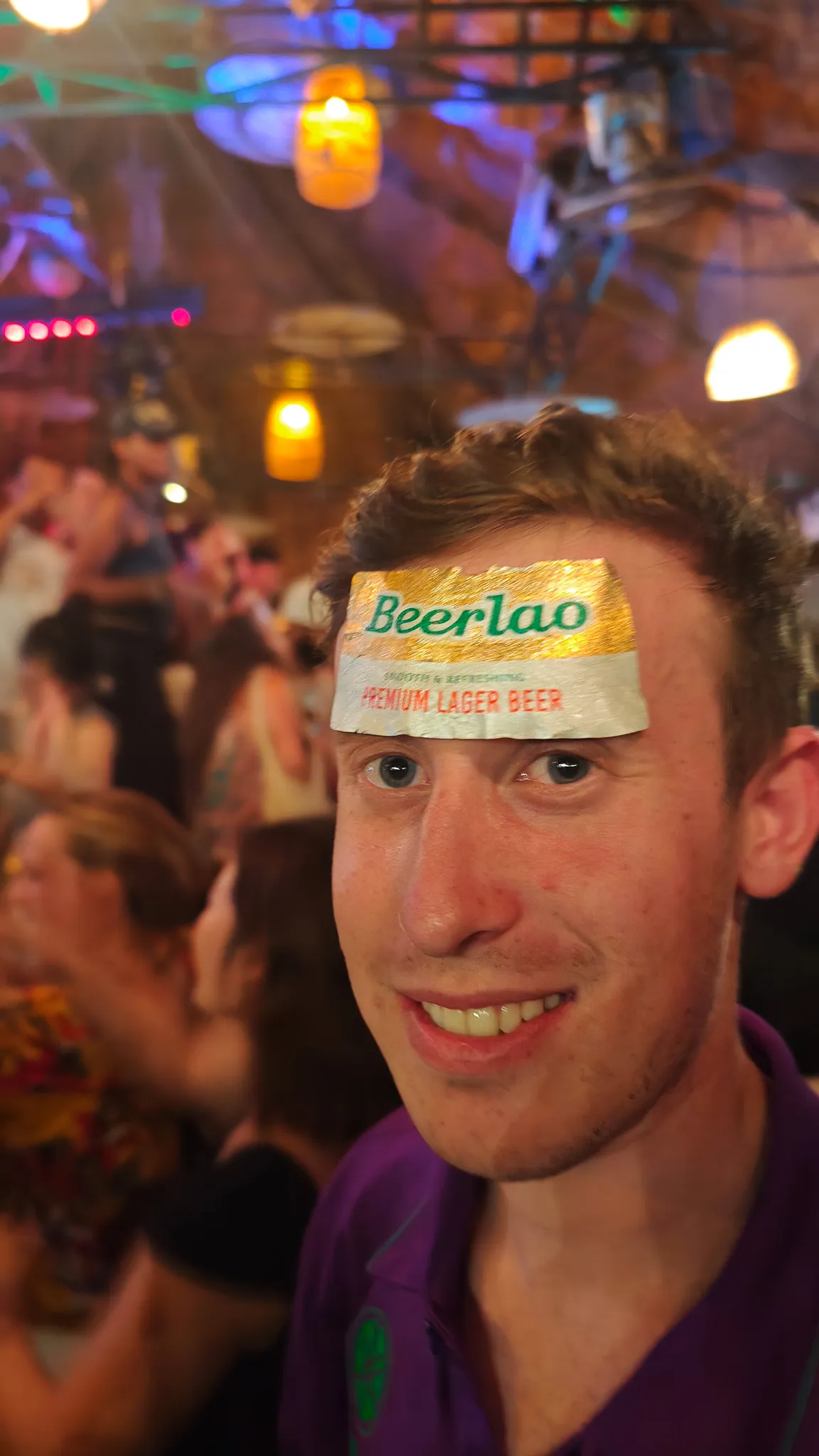 Young man with a Beer Lao label stuck on his forehead at a packed bar during the Vang Vieng pub crawl