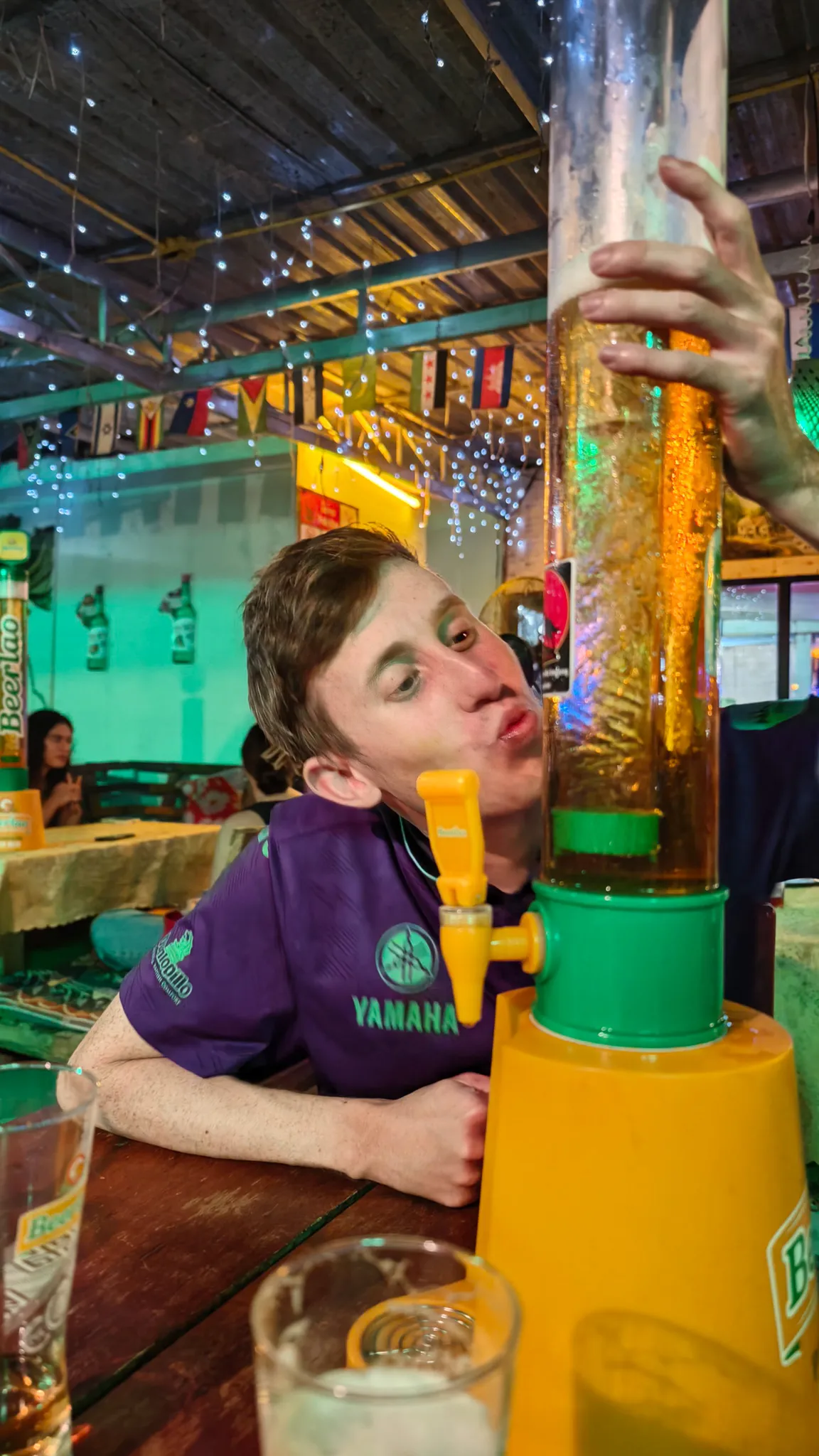 Young man with a Beer Lao beer tower dispenser at a neon-lit bar during the Vang Vieng pub crawl