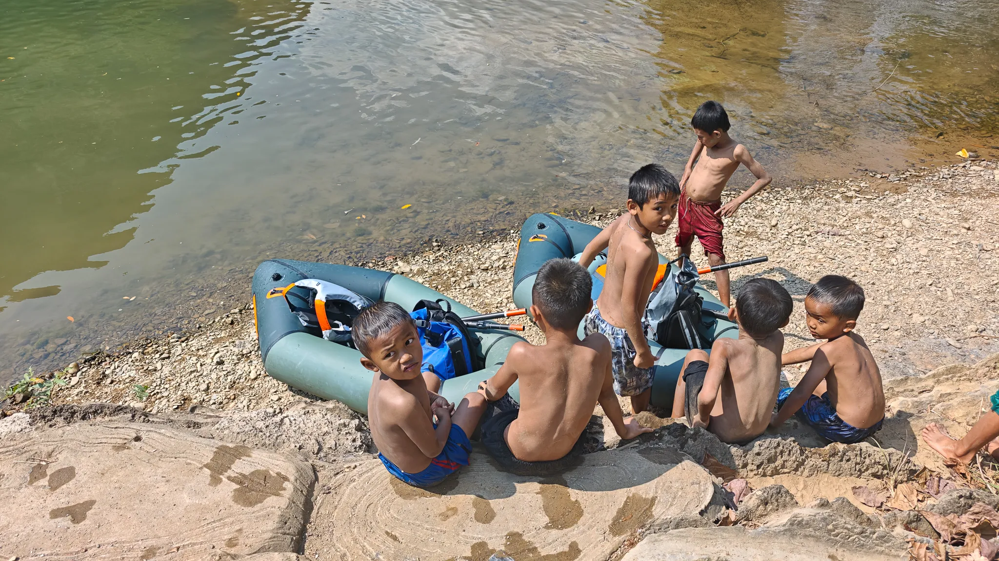 Group of local children playing around a beached packraft on the Nam Song riverbank in Vang Vieng