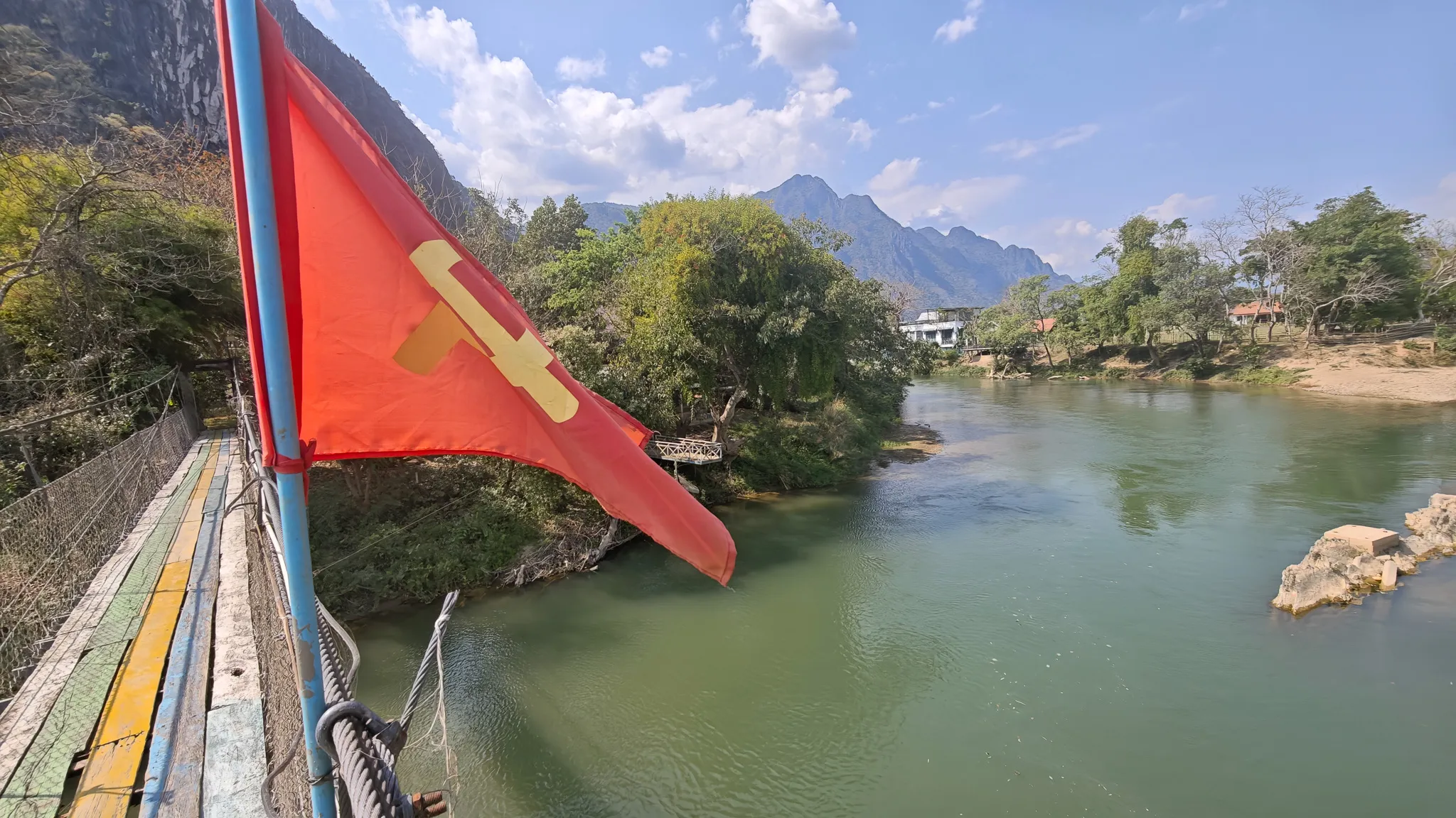 Red communist party flag with hammer and sickle on a suspension bridge over the Nam Song River in Vang Vieng