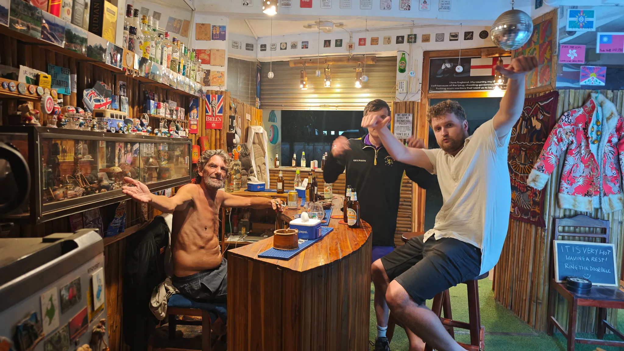 Three friends at the bar inside a memorabilia-packed dive bar with disco ball and England flag in Vang Vieng