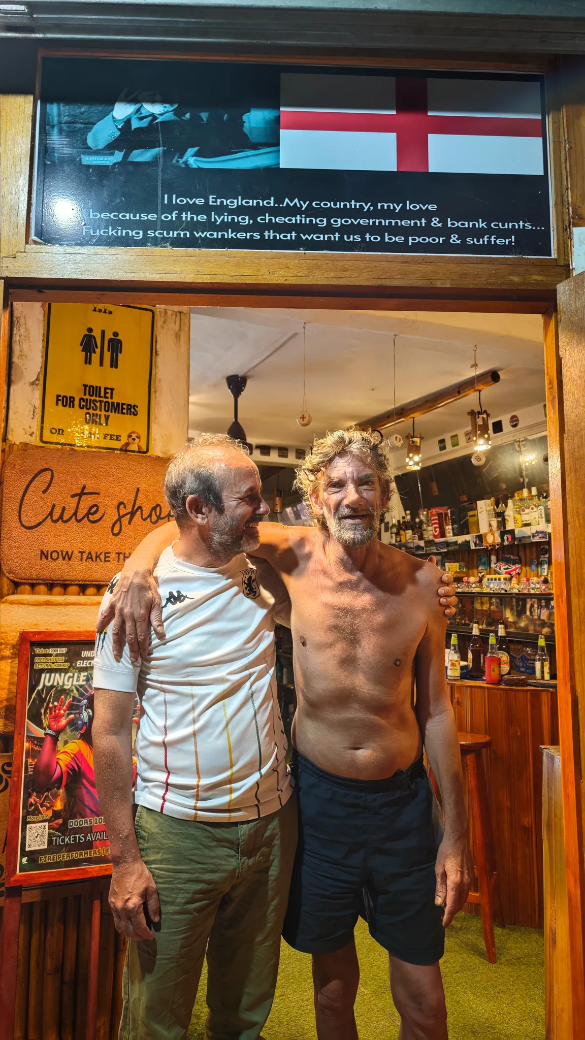 Two friends at a Vang Vieng bar with a Keep Quiet Respect the Temple sign and tequila calling doorway