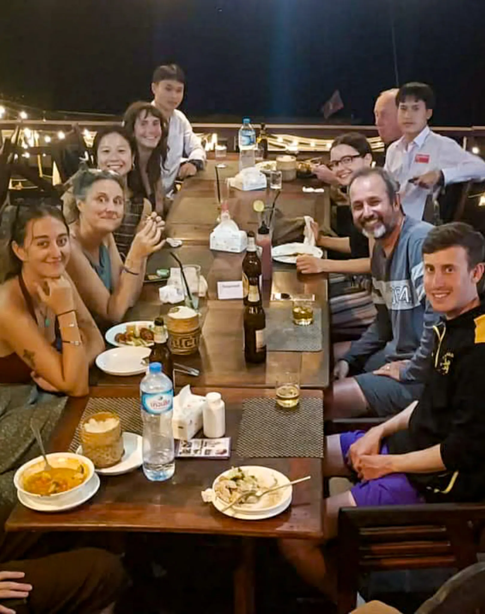 Portrait view of friends around a dinner table with Lao curry and Beer Lao at an open-air restaurant in Vang Vieng