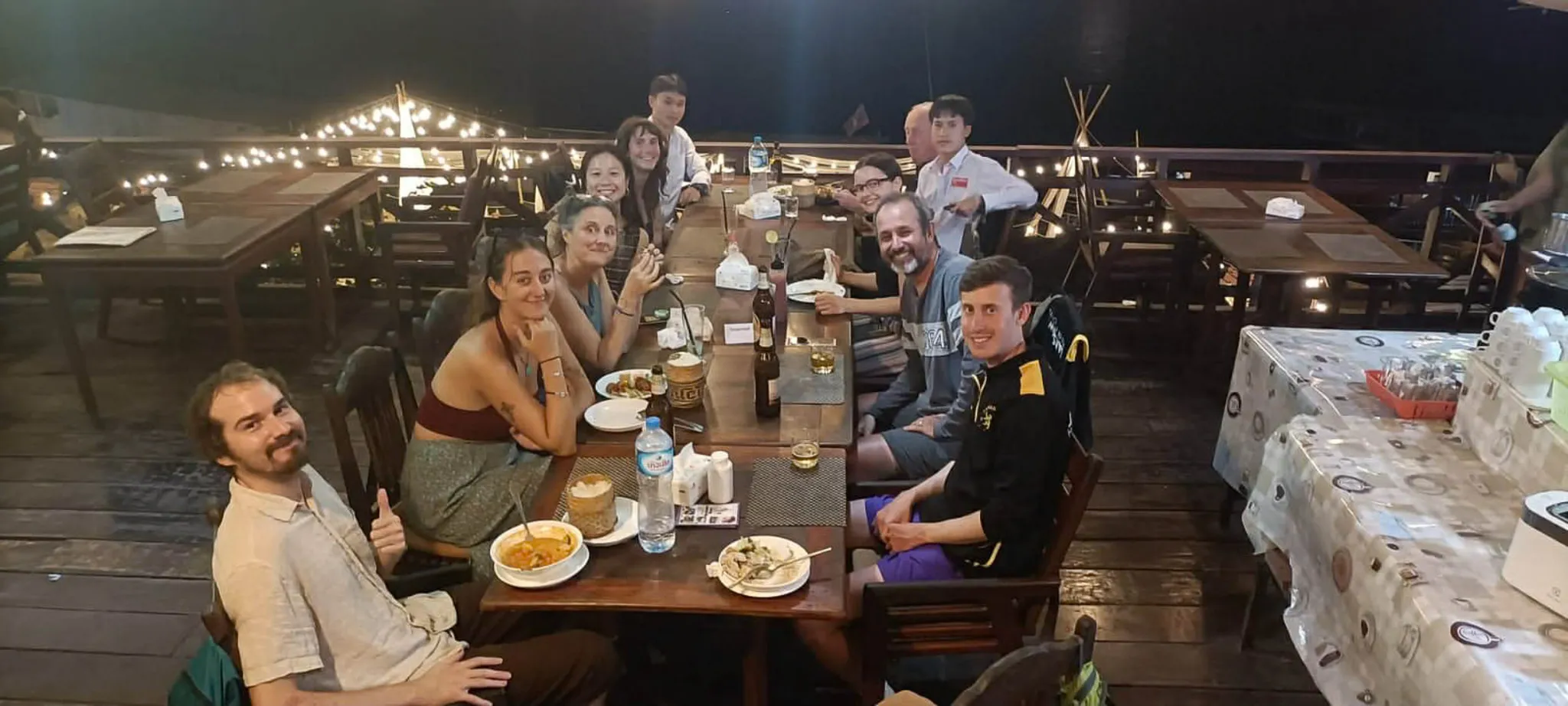 Group of friends enjoying dinner with Lao food and Beer Lao at a riverside restaurant in Vang Vieng with fairy lights
