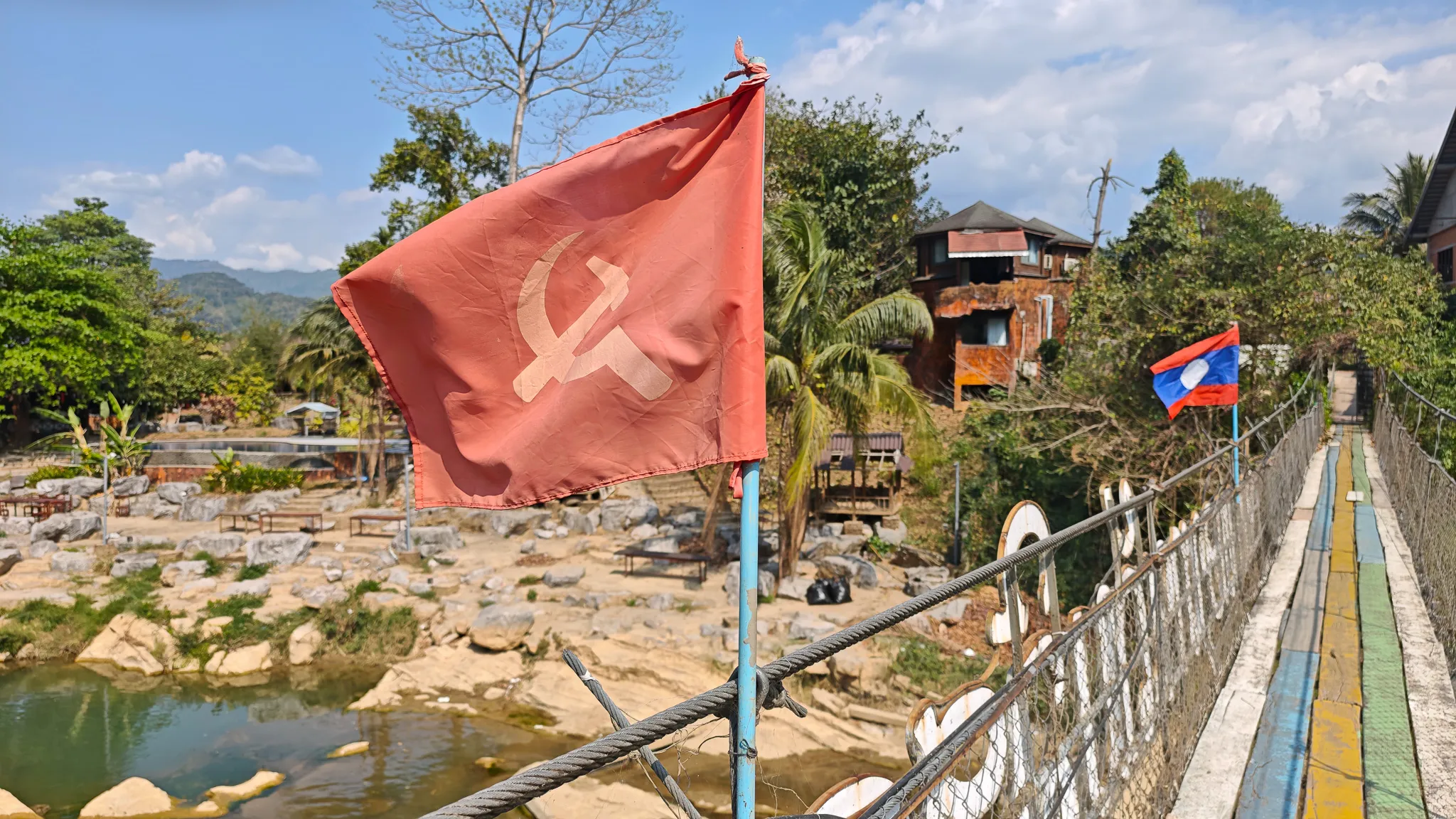 Communist hammer and sickle flag on a suspension bridge with Laos flag in background over the Nam Song River