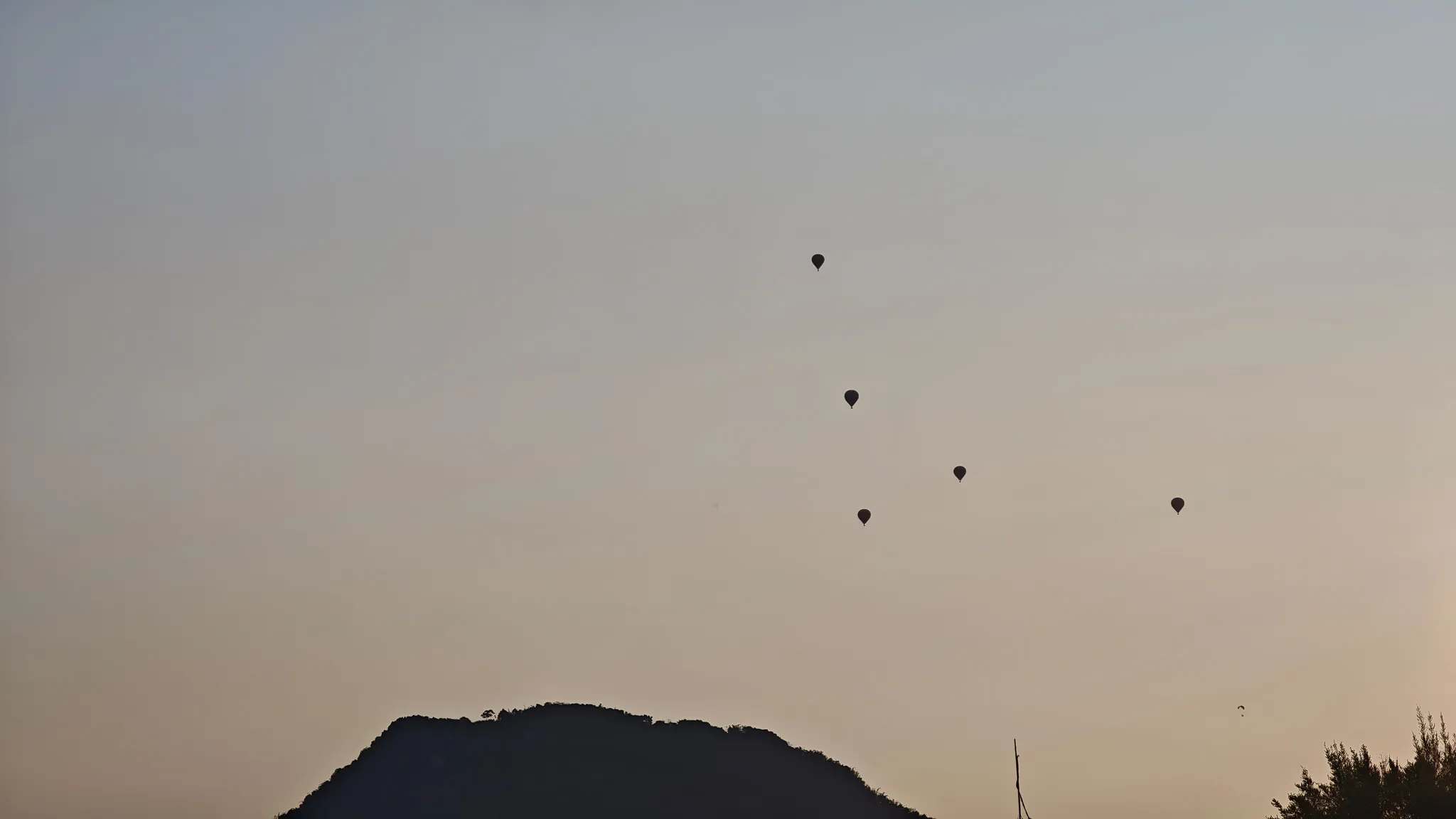 Silhouettes of five hot air balloons floating above a mountain at dusk in Vang Vieng