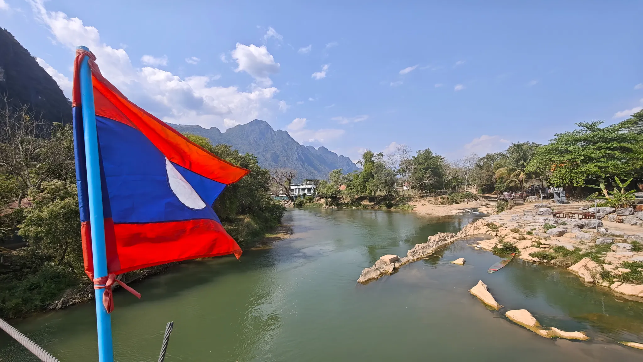Laos flag on a bridge overlooking the Nam Song River with karst limestone peaks and lush greenery in Vang Vieng
