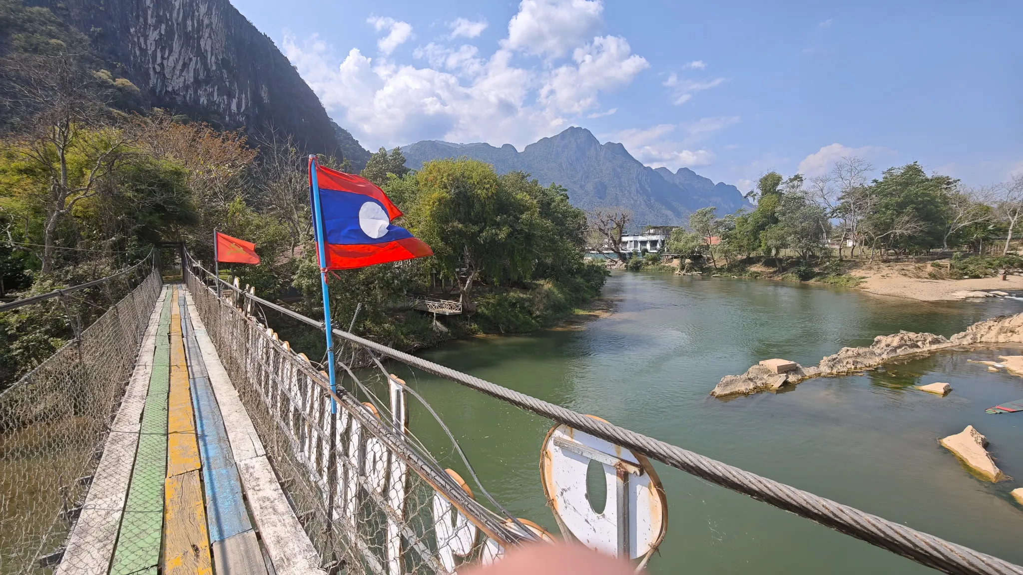 Laos flag on a colourful pedestrian bridge walkway with limestone karsts and river below in Vang Vieng