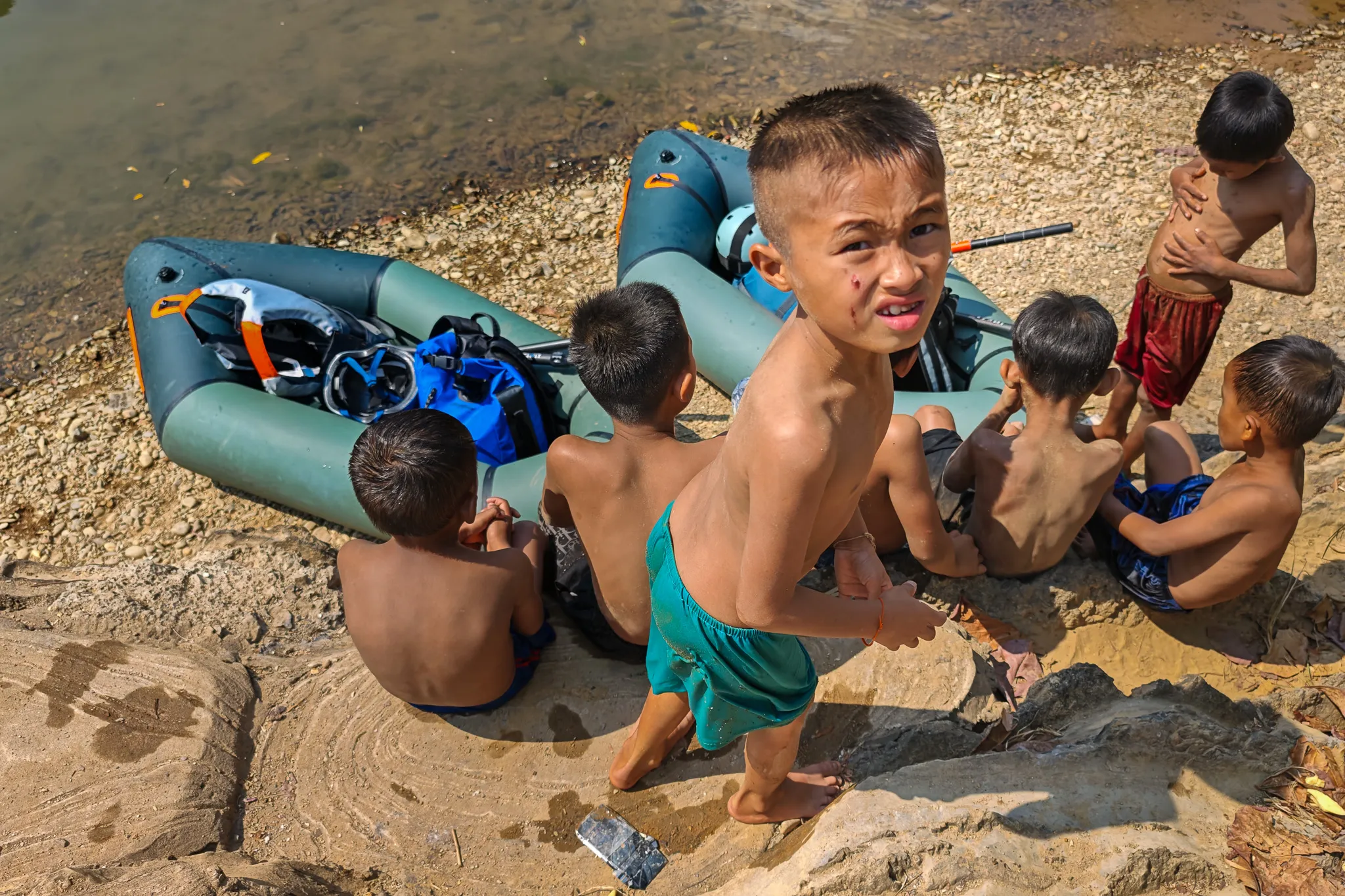 Local Lao children gathered around a packraft pulled onto the sandy riverbank of the Nam Song River in Vang Vieng