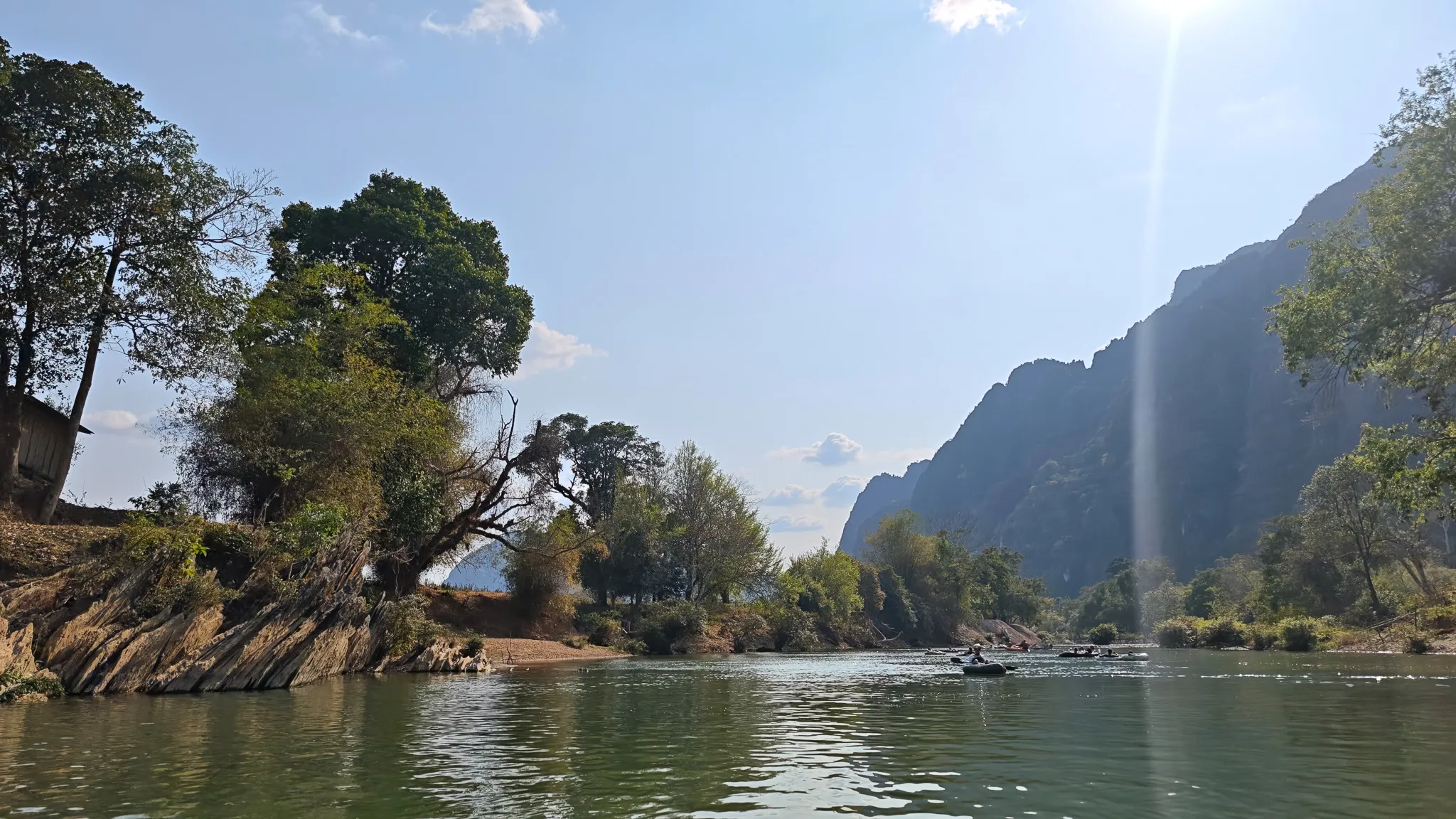 Packrafting the Nam Song River past dramatic karst limestone cliffs with boats in the distance