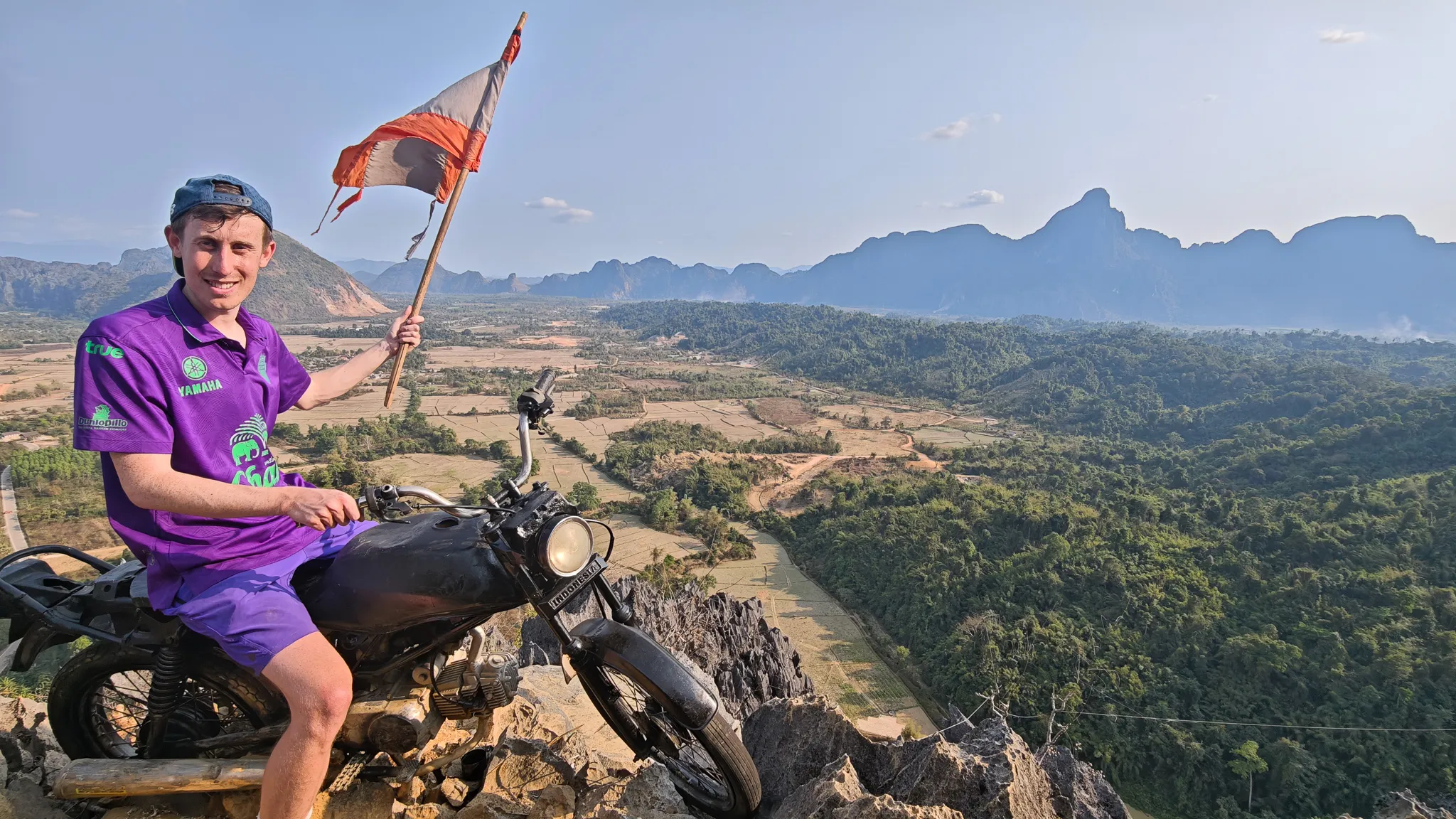 Person sitting on a motorcycle at the Nam Xay viewpoint summit at golden hour with misty karst mountains