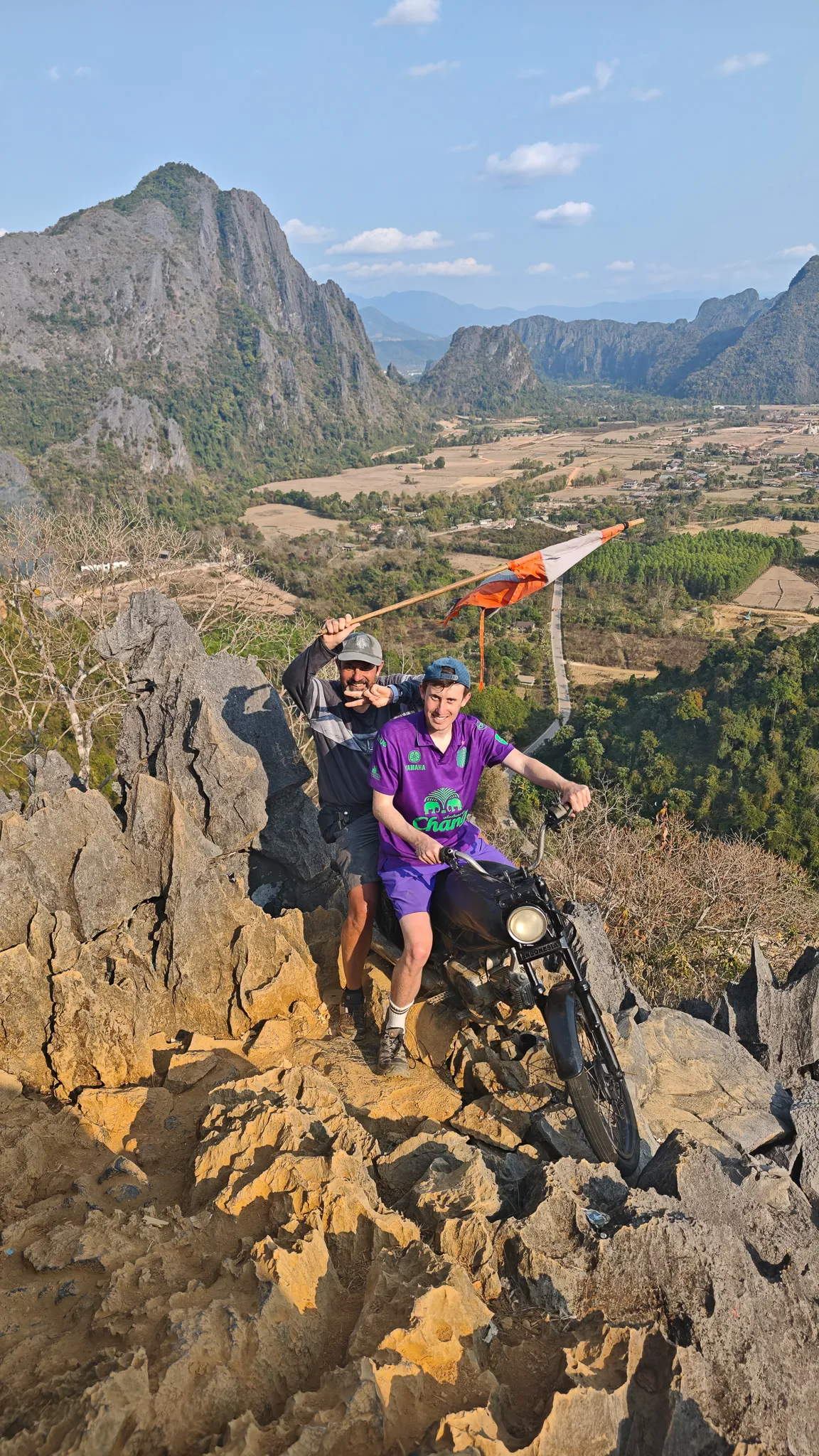 Friends sitting on jagged limestone rocks at the Nam Xay summit with flag and mountain views