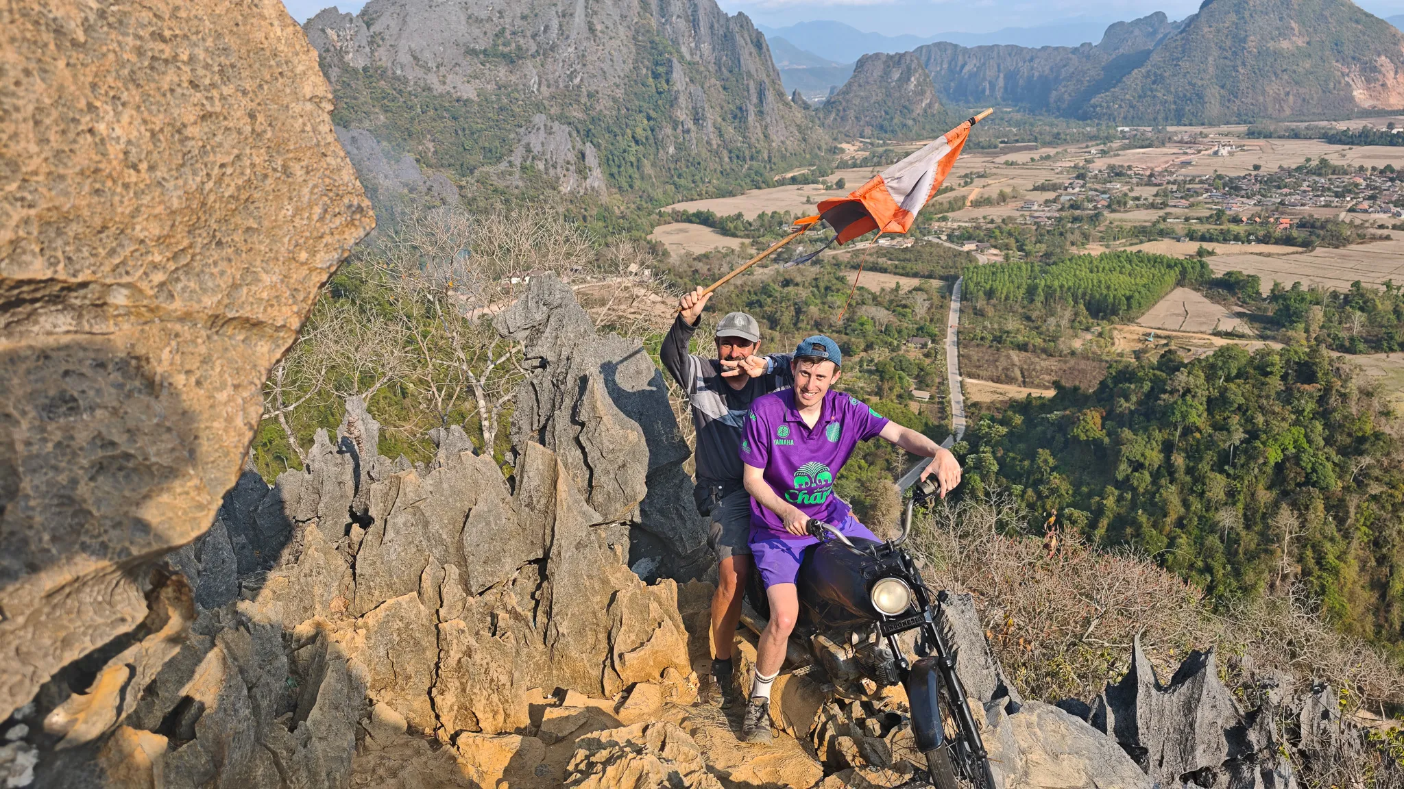 Two friends waving and posing at the Nam Xay viewpoint summit with karst mountains behind