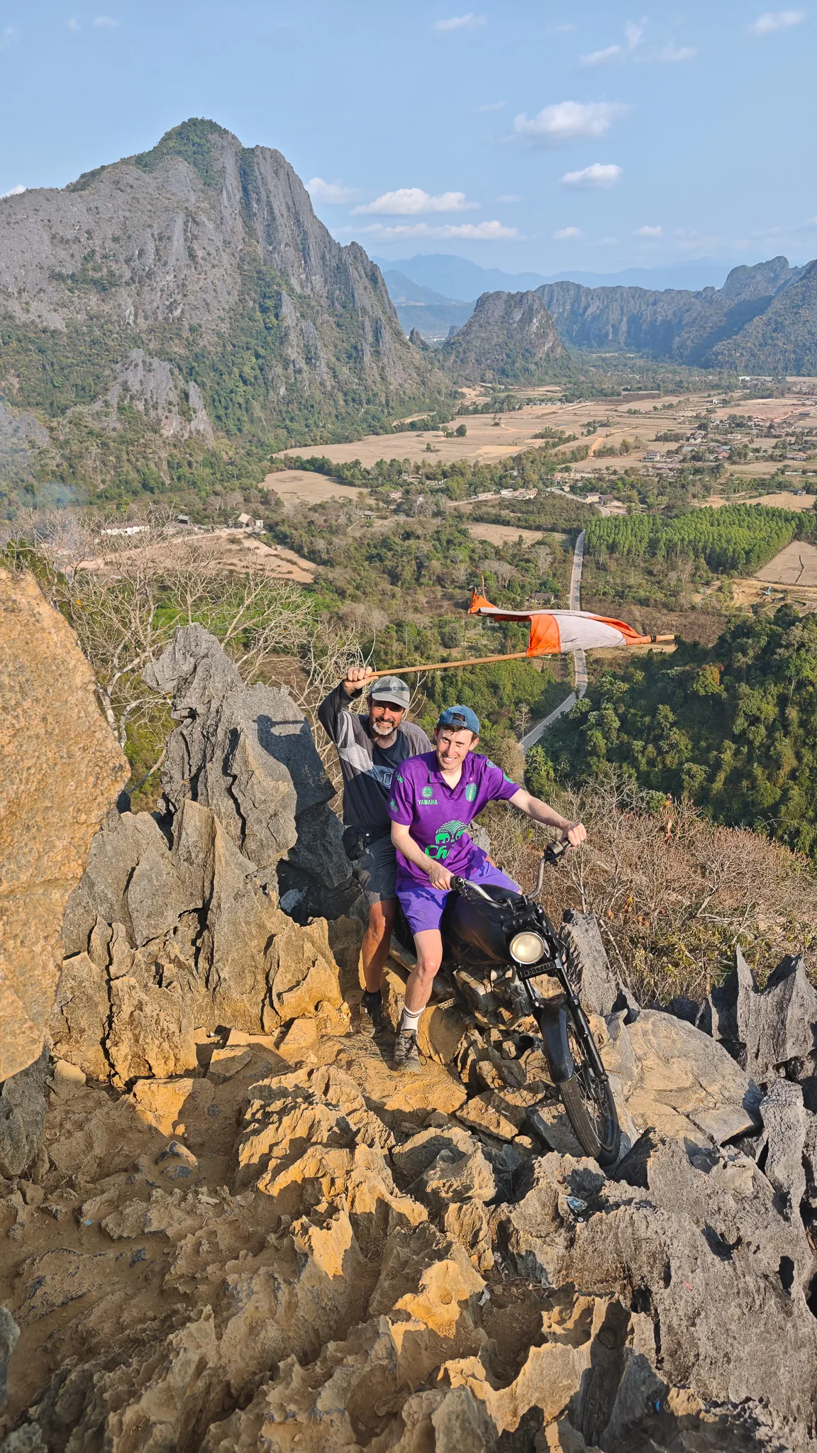 Friends waving the Laos flag on the rocky summit of Nam Xay viewpoint overlooking the valley
