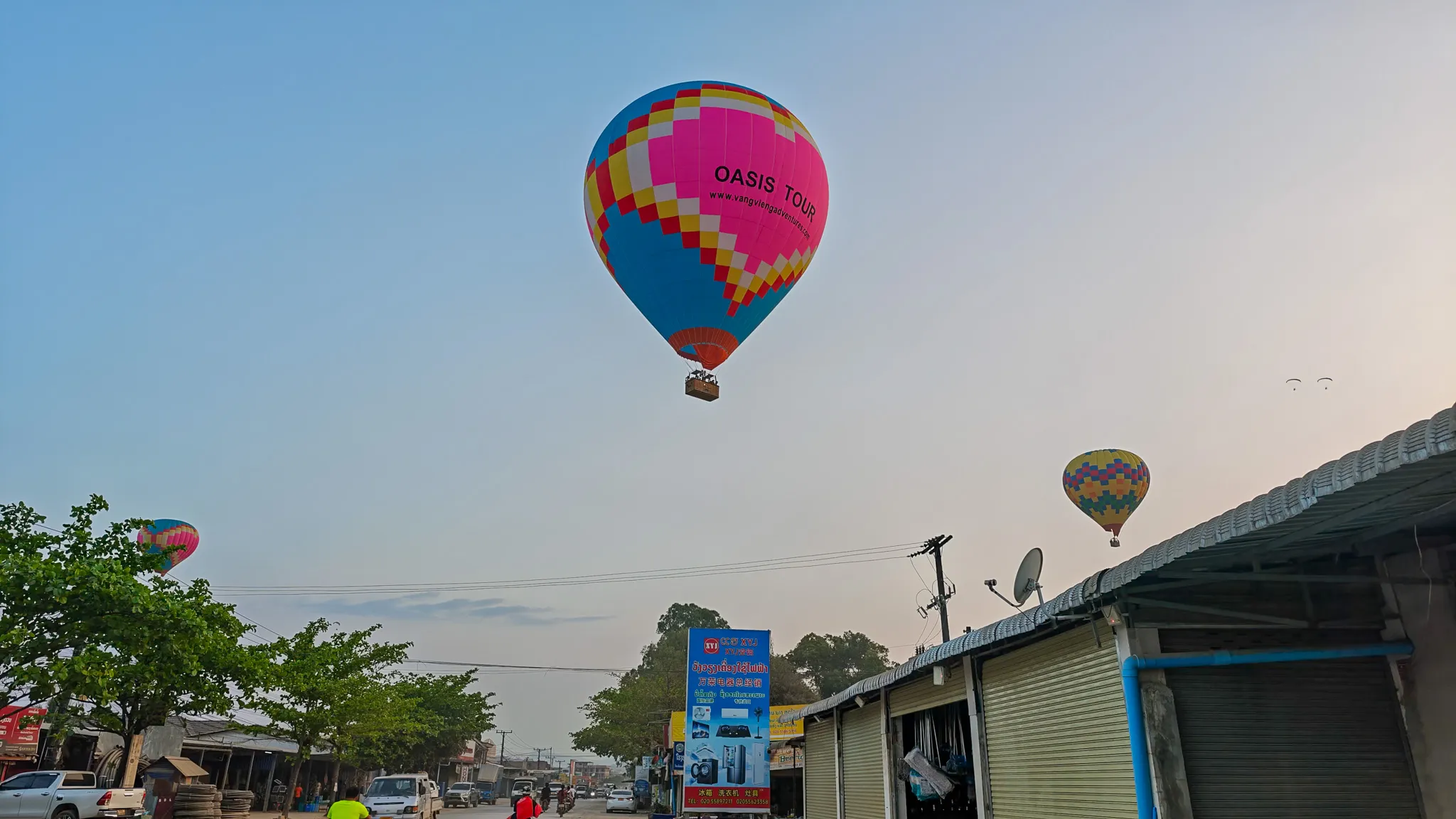 Colourful Oasis Tour hot air balloon flying low over the main street in Vang Vieng with shops below