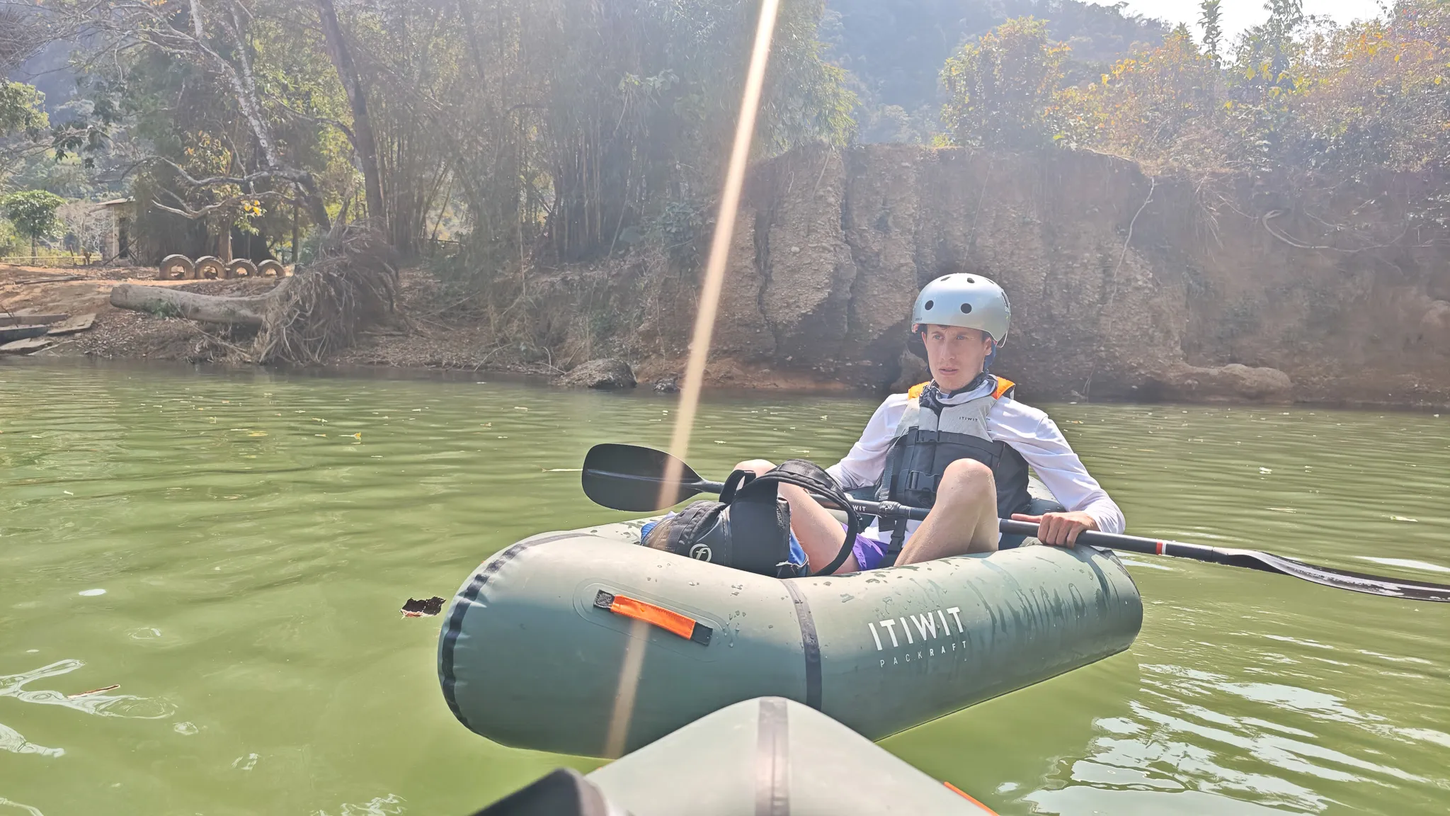 Packrafter in an Itiwit packraft with helmet and life jacket paddling the Nam Song River in Vang Vieng with limestone cliffs behind