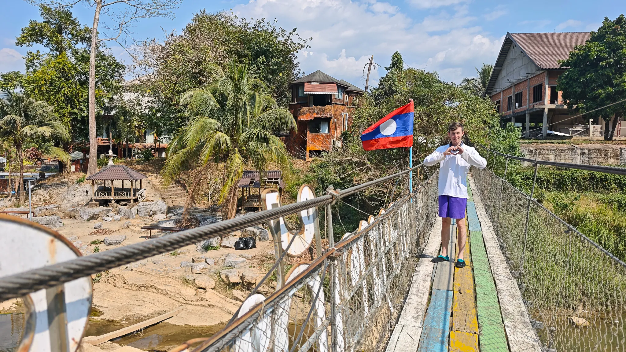 Person standing on a colourful suspension bridge with a Laos flag over the Nam Song River in Vang Vieng