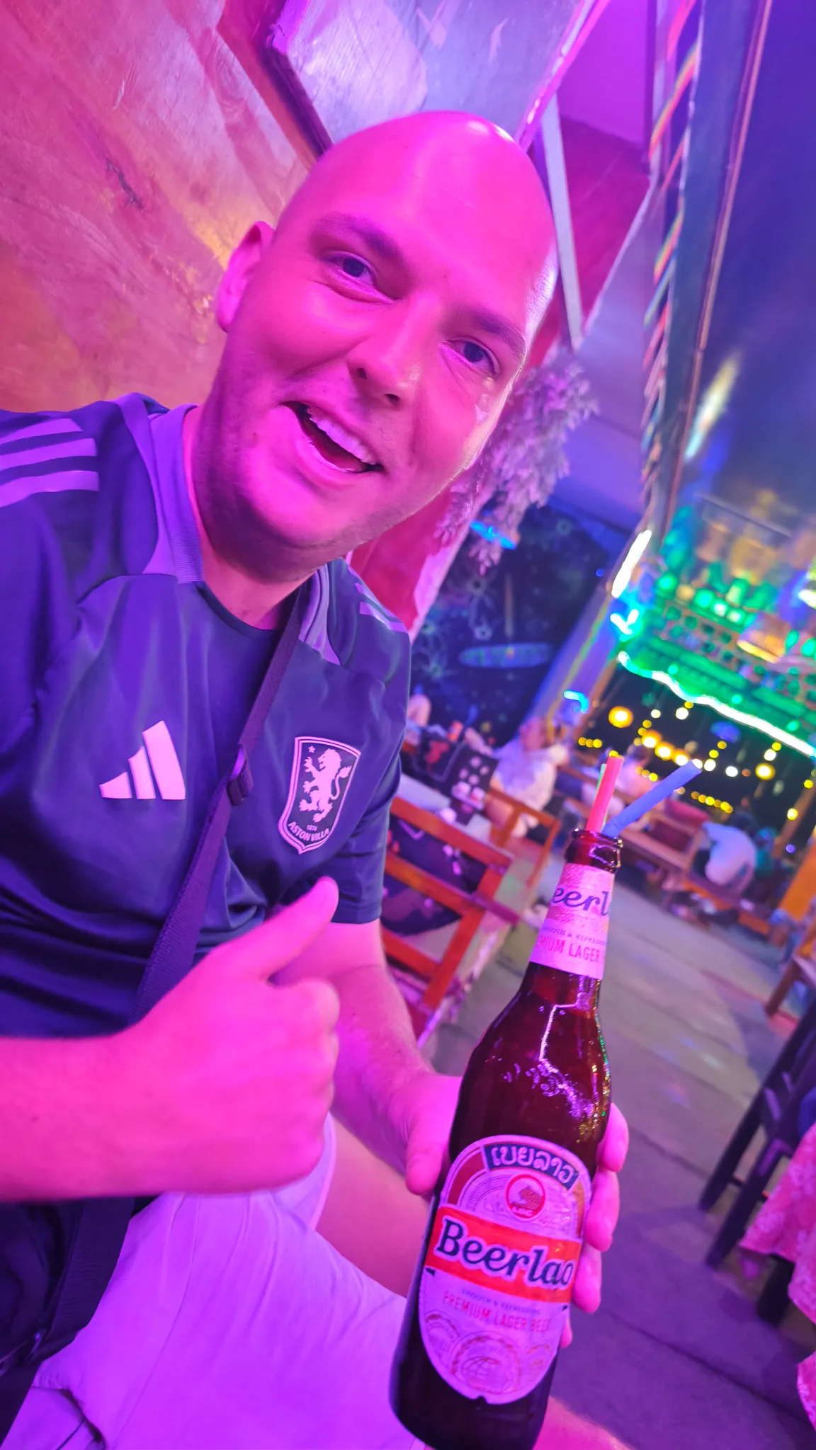 Selfie with a Beer Lao bottle wearing an Aston Villa shirt at a colourful neon bar in Vang Vieng