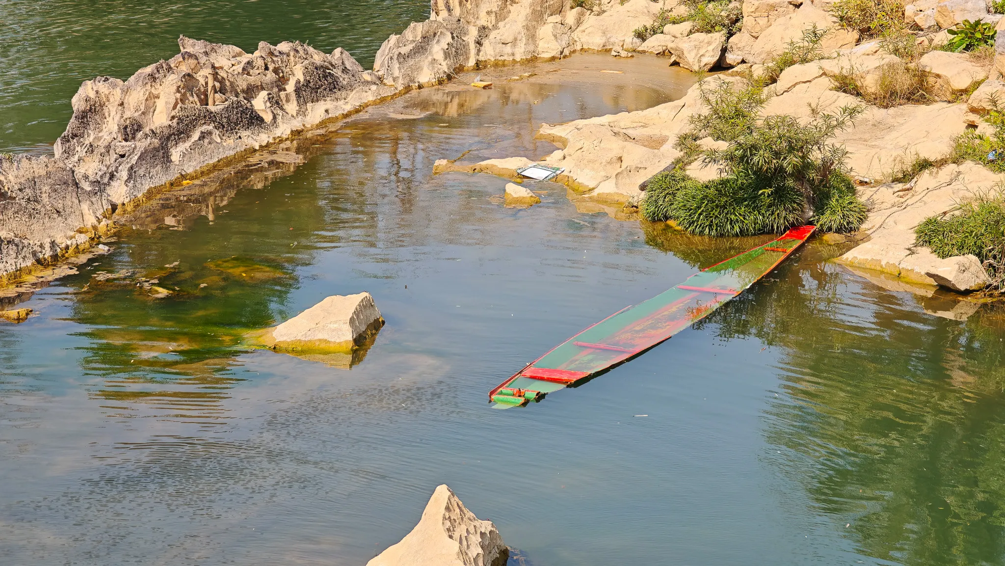 Sunken colourful longboat among the rocks in the shallow Nam Song River in Vang Vieng