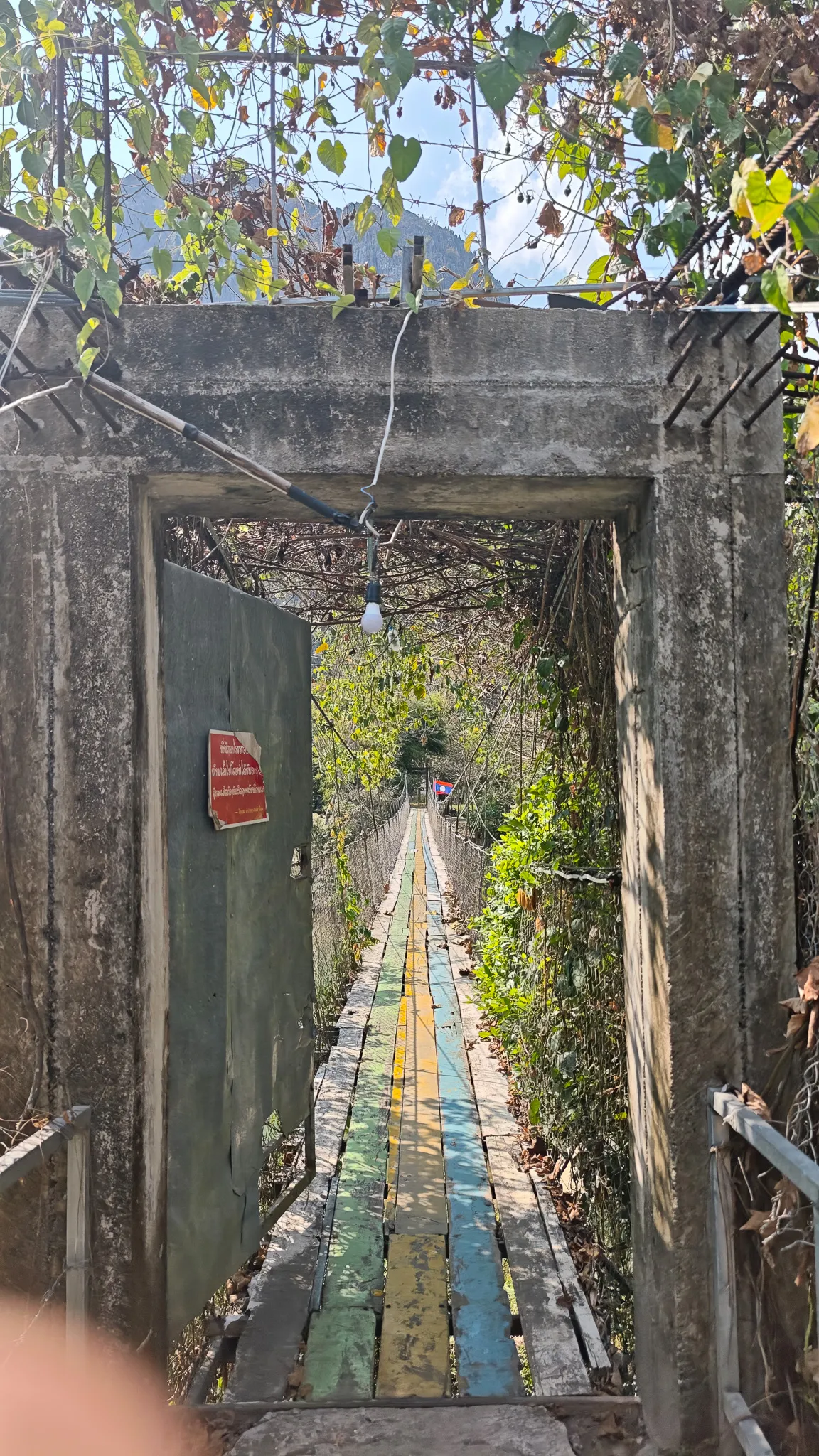 Rainbow-painted walkway of a suspension bridge over the Nam Song River in Vang Vieng with mountains beyond