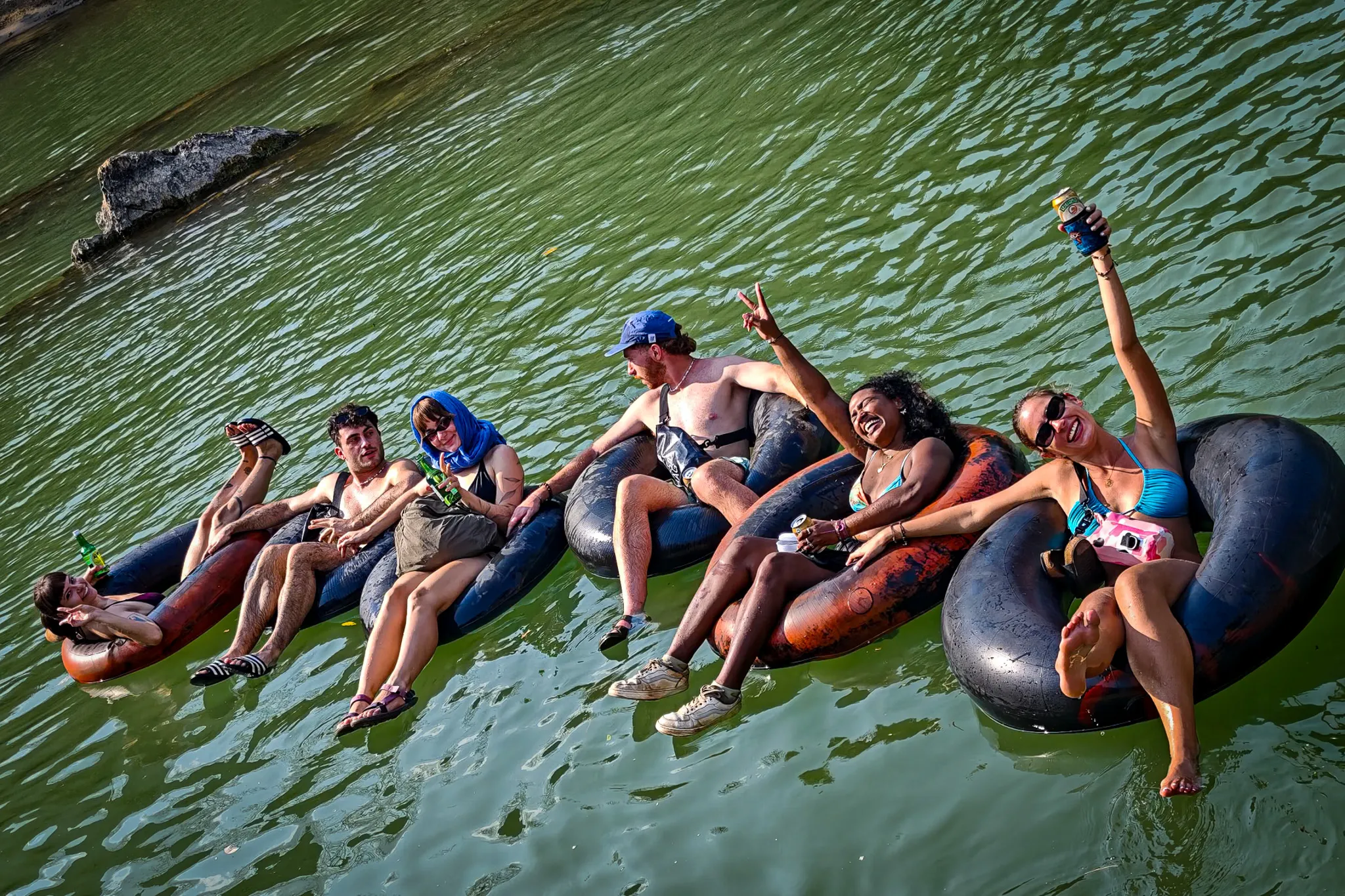 Group of tipsy tubers on inner tubes drinking beers and celebrating as they float down the Nam Song River