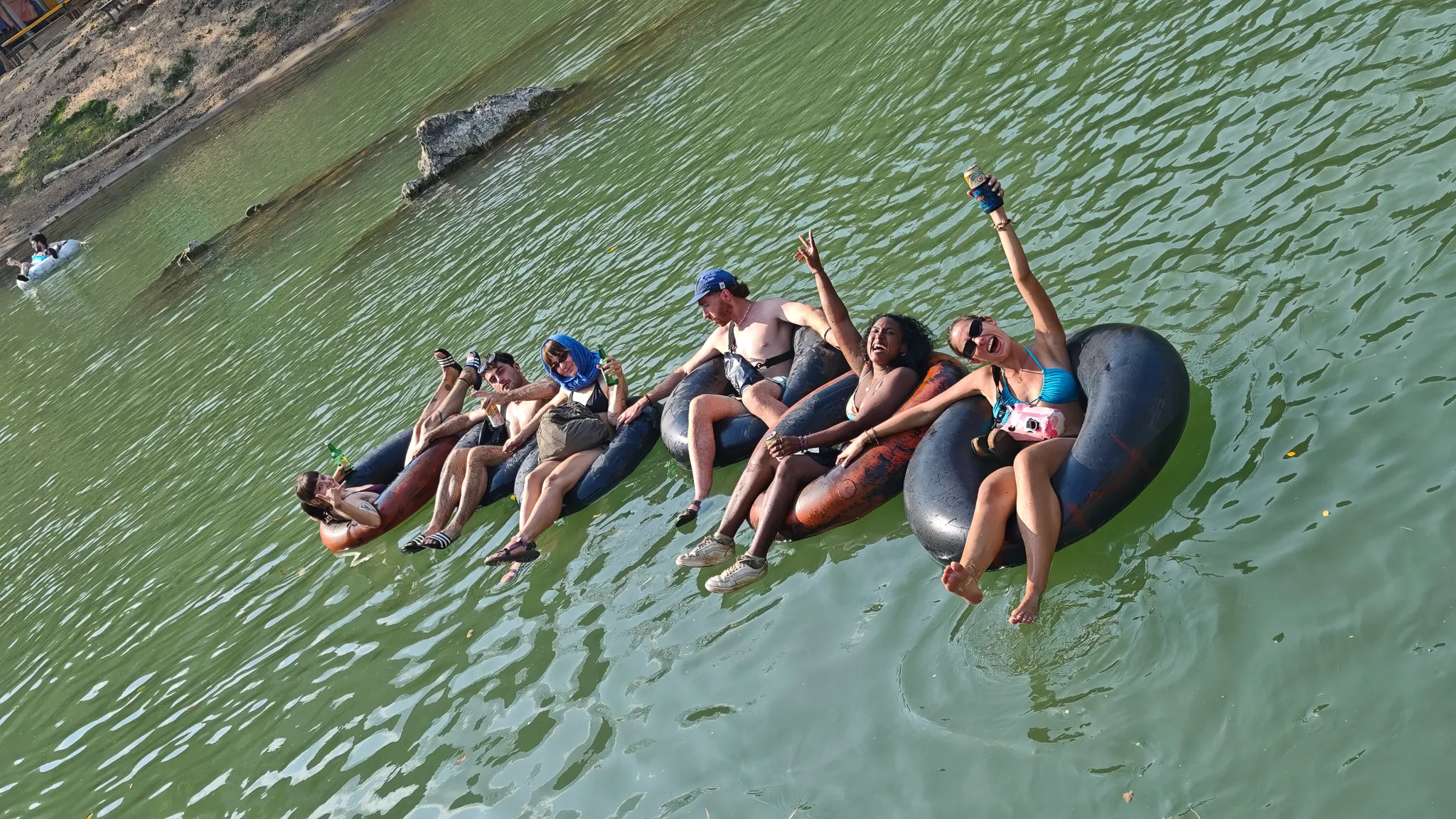 Five tubers linked together on inner tubes floating the Nam Song River with beers in hand in Vang Vieng