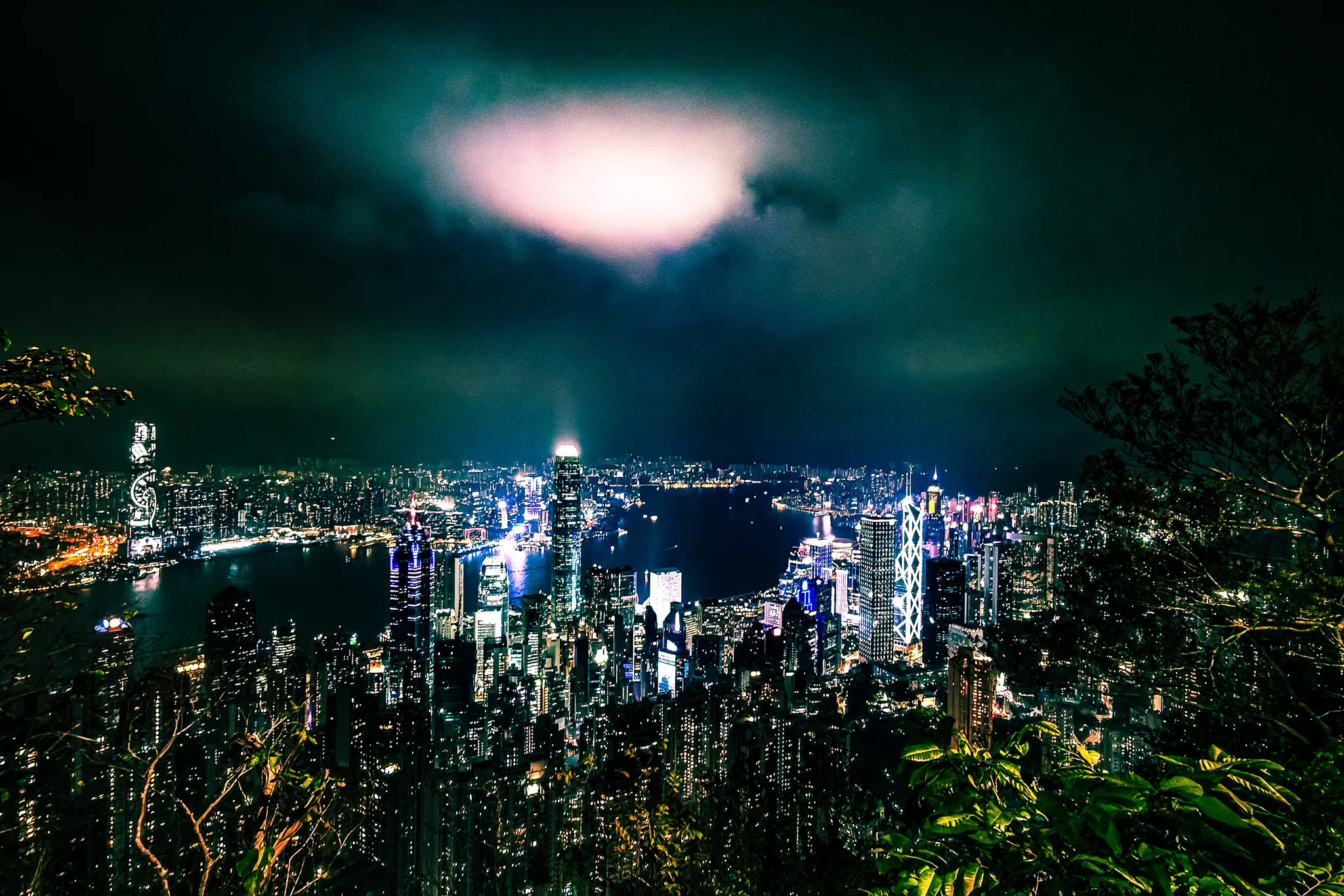 Wide-angle night view from Victoria Peak with Hong Kong skyscrapers, harbour and Kowloon lit up below dramatic clouds