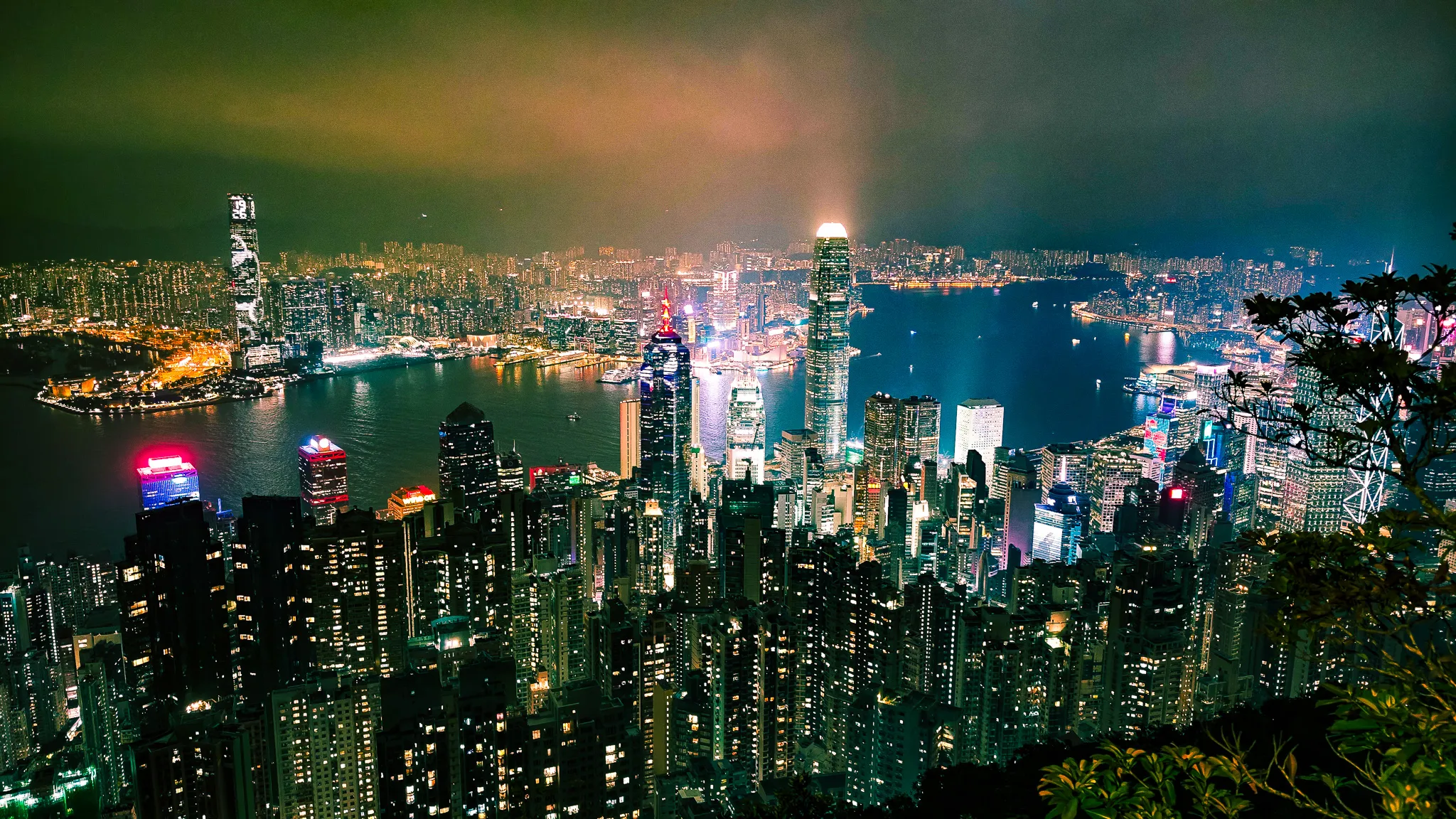 ICC tower in Kowloon displaying a Welcome sign viewed from Victoria Peak at night with the harbour below
