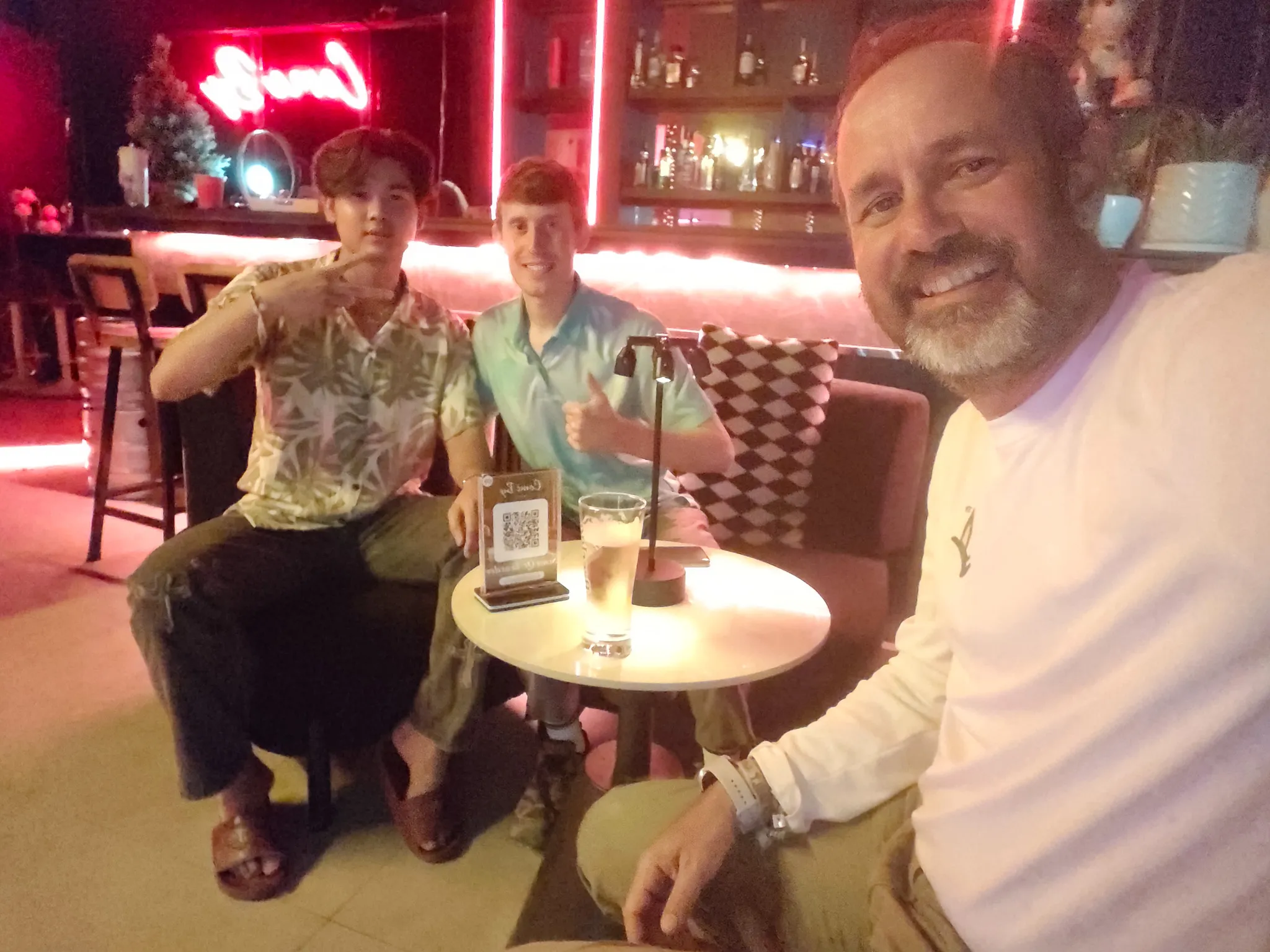 Selfie with two friends at a neon-lit cocktail bar in Vientiane with drinks on a small round table