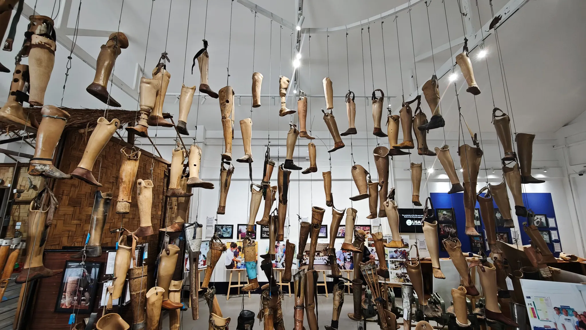 Wide view of the COPE Centre exhibition hall with prosthetic legs suspended from ceiling and information displays about UXO clearance