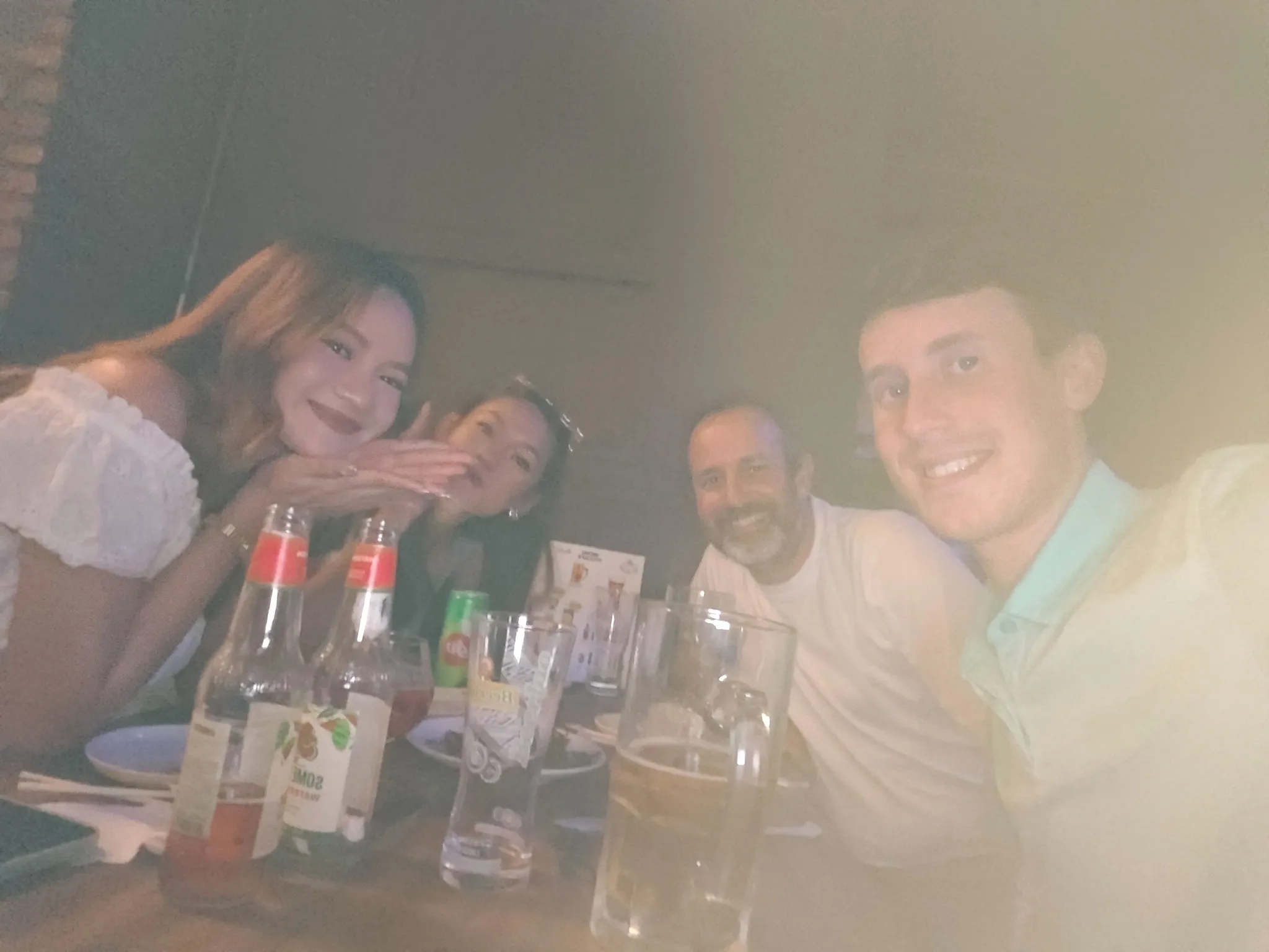 Group selfie of four friends smiling over dinner with Beer Lao and drinks in Vientiane
